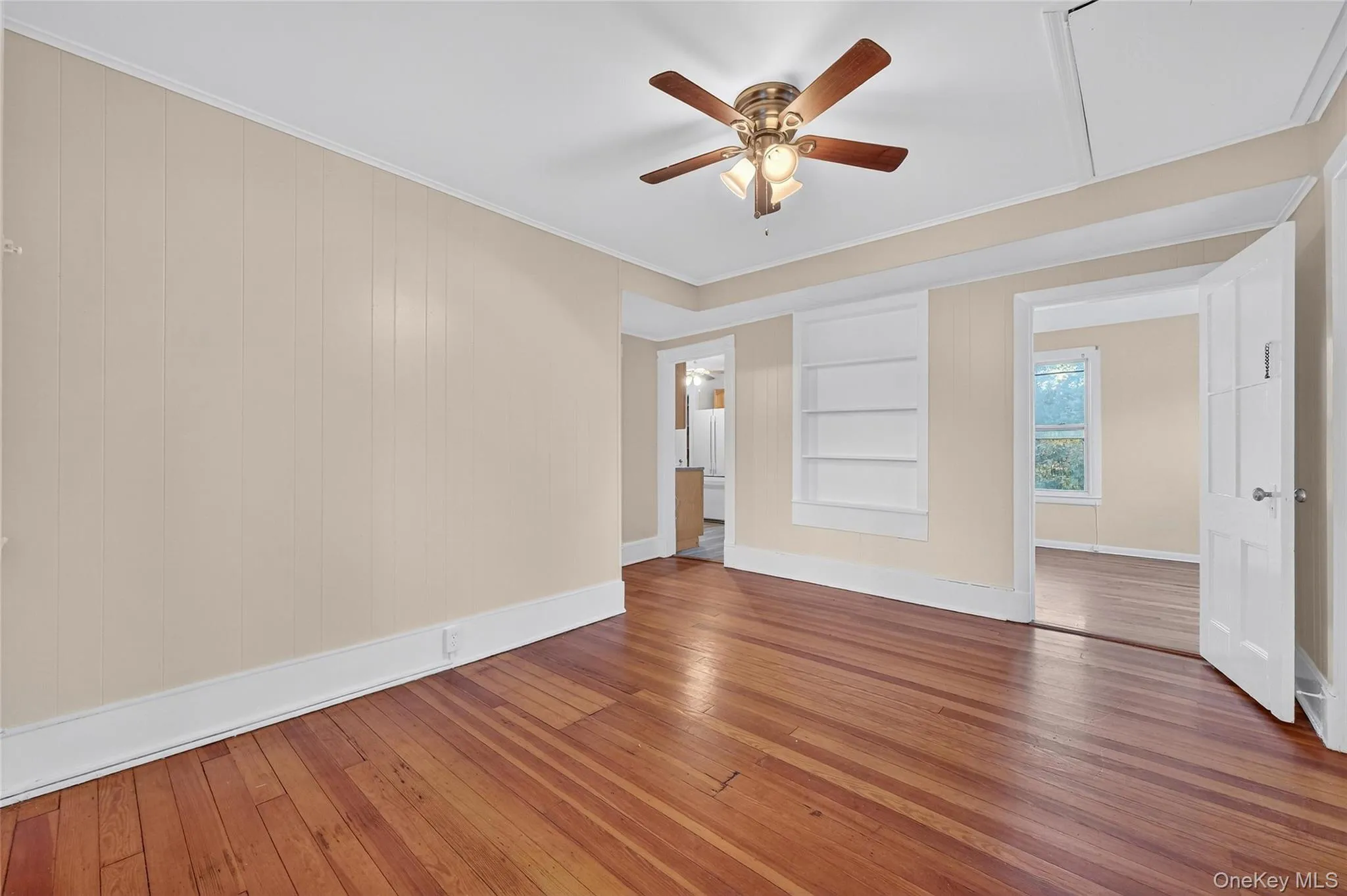 Empty room with wood-type flooring, built in shelves, ornamental molding, attic access, and ceiling fan Empty room with wood-type flooring, built in shelves, ornamental molding, attic access, and ceiling fan