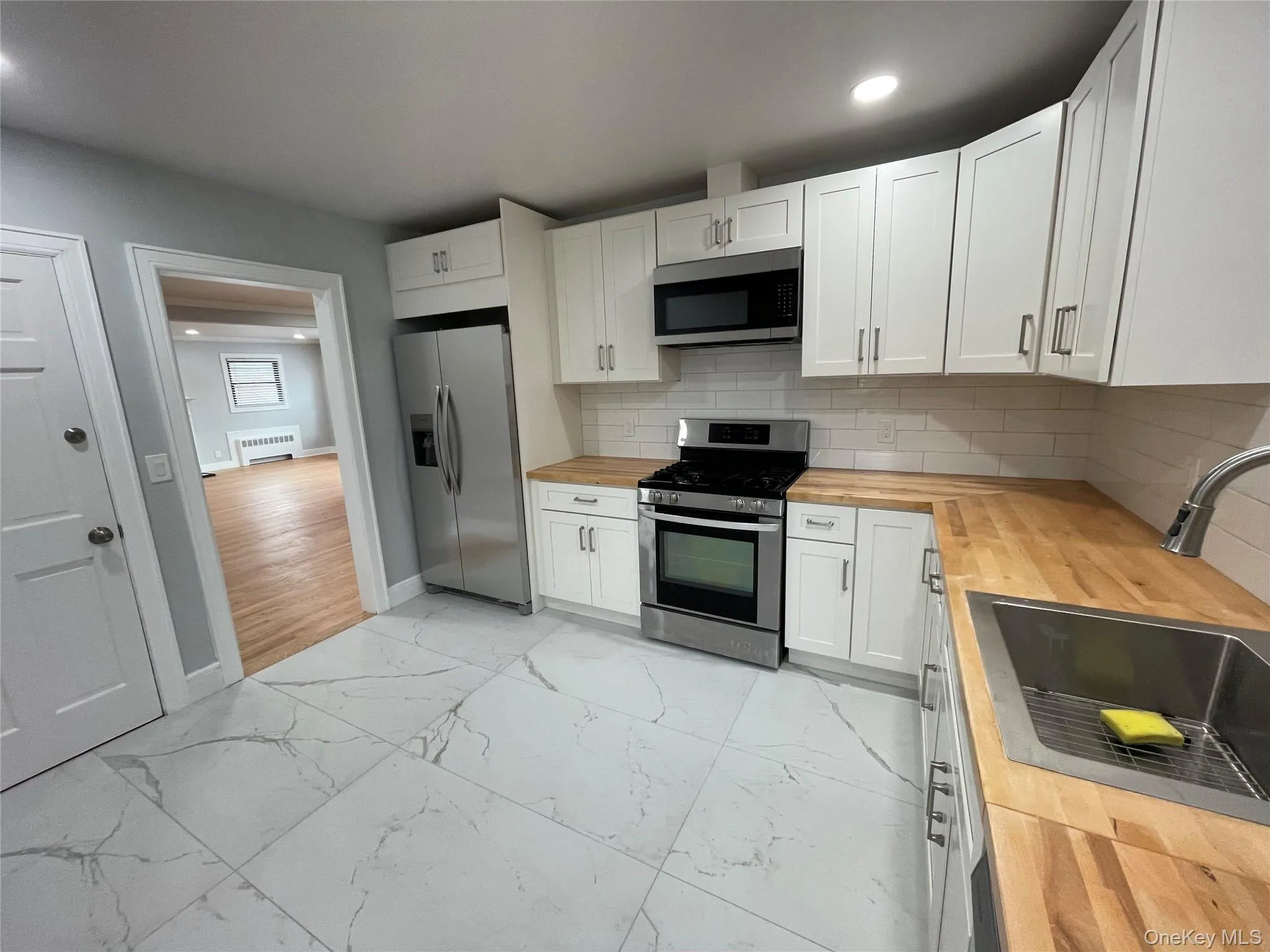 Kitchen with wood counters, white cabinetry, appliances with stainless steel finishes, backsplash, and recessed lighting Kitchen with wood counters, white cabinetry, appliances with stainless steel finishes, backsplash, and recessed lighting