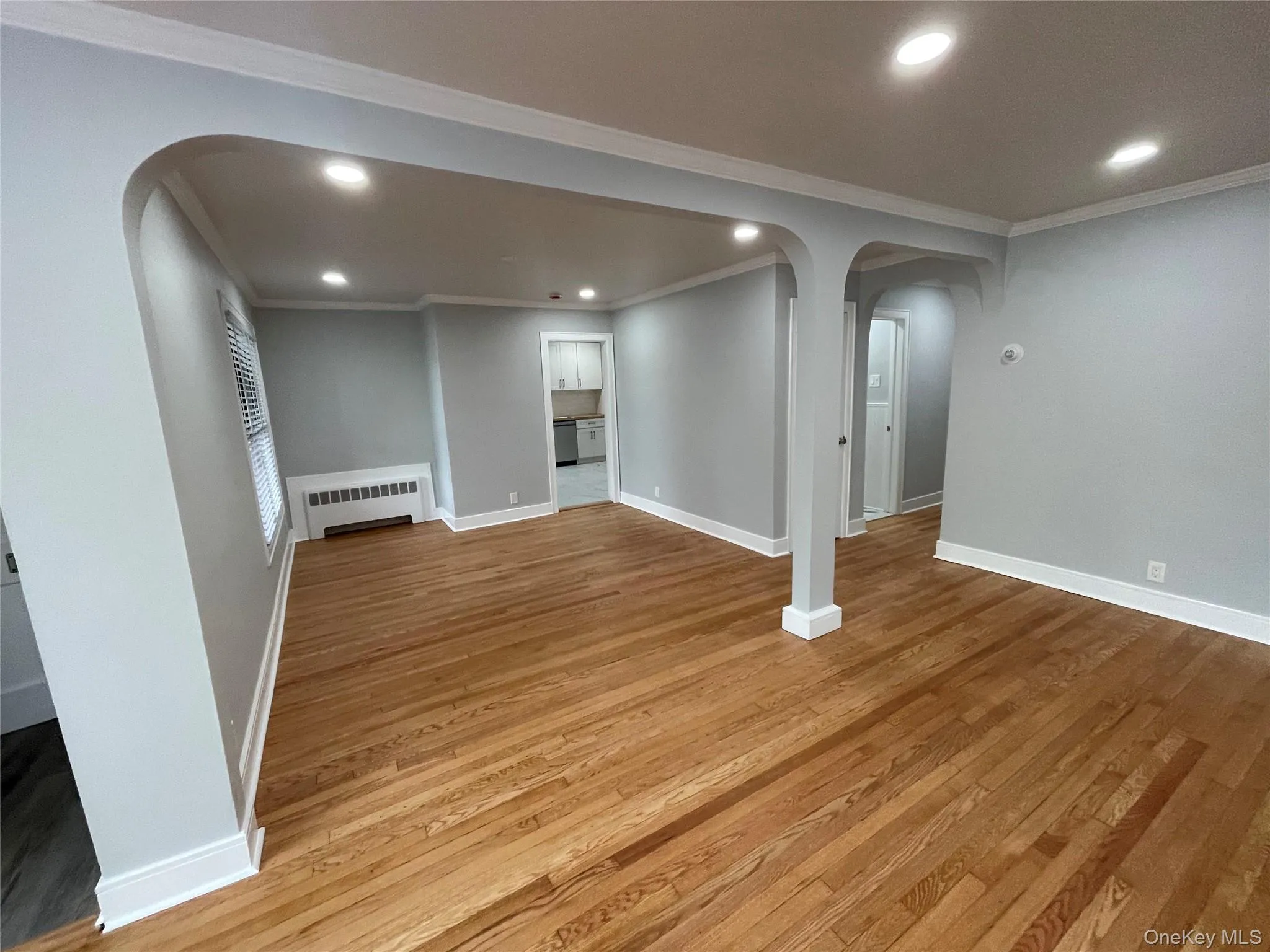 Basement with arched walkways, recessed lighting, ornamental molding, light wood-style flooring, and radiator heating unit Basement with arched walkways, recessed lighting, ornamental molding, light wood-style flooring, and radiator heating unit