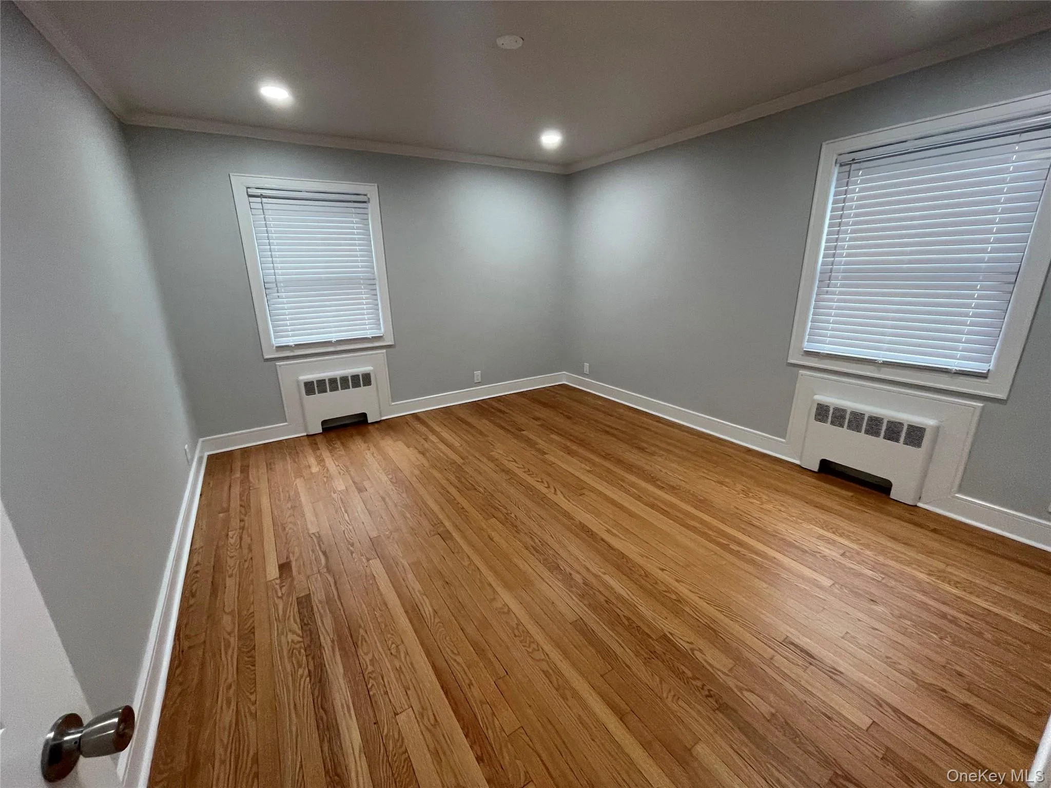 Empty room with ornamental molding, radiator, light wood-style floors, and recessed lighting Empty room with ornamental molding, radiator, light wood-style floors, and recessed lighting