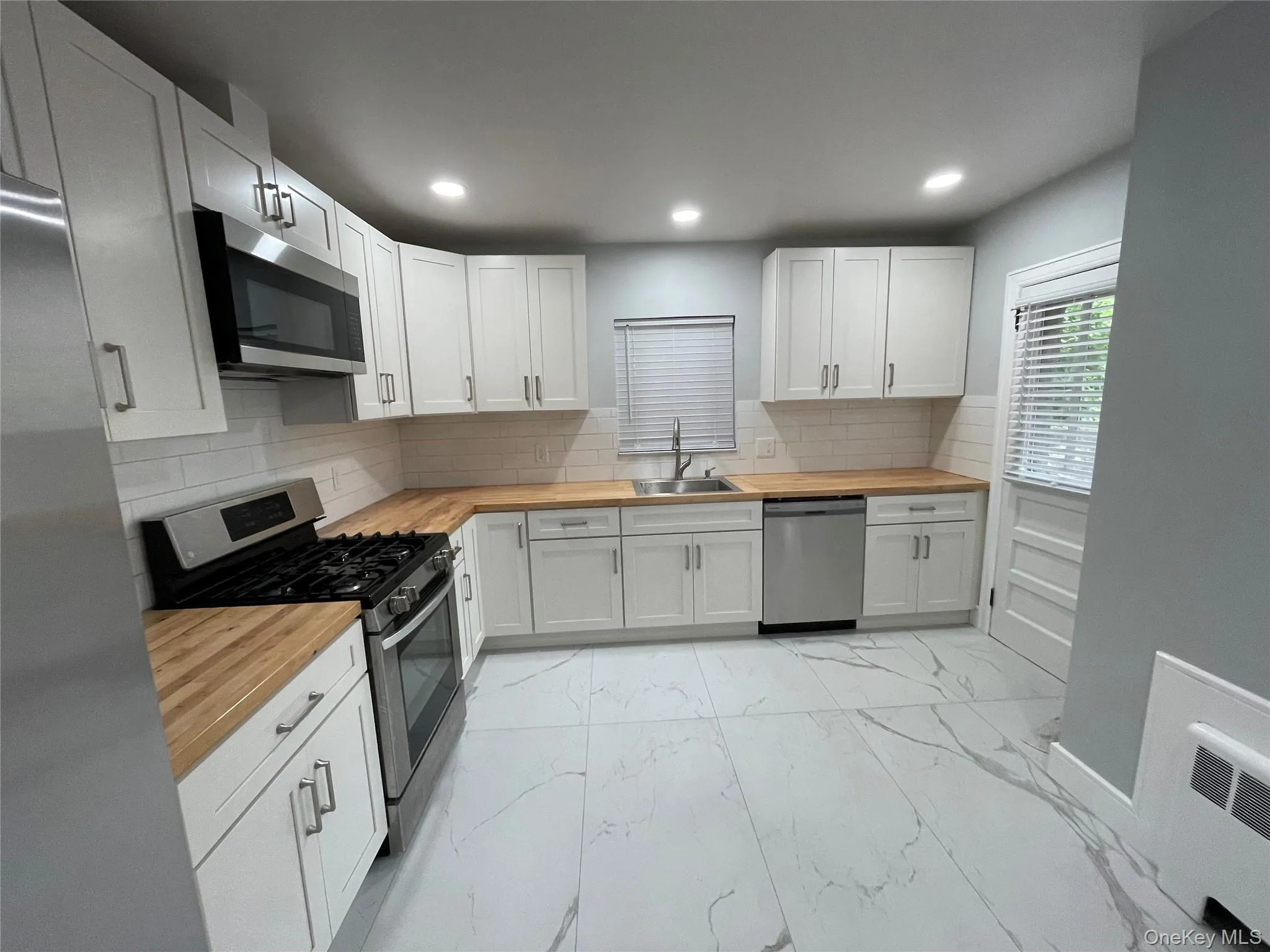 Kitchen with appliances with stainless steel finishes, butcher block counters, backsplash, white cabinets, and recessed lighting Kitchen with appliances with stainless steel finishes, butcher block counters, backsplash, white cabinets, and recessed lighting