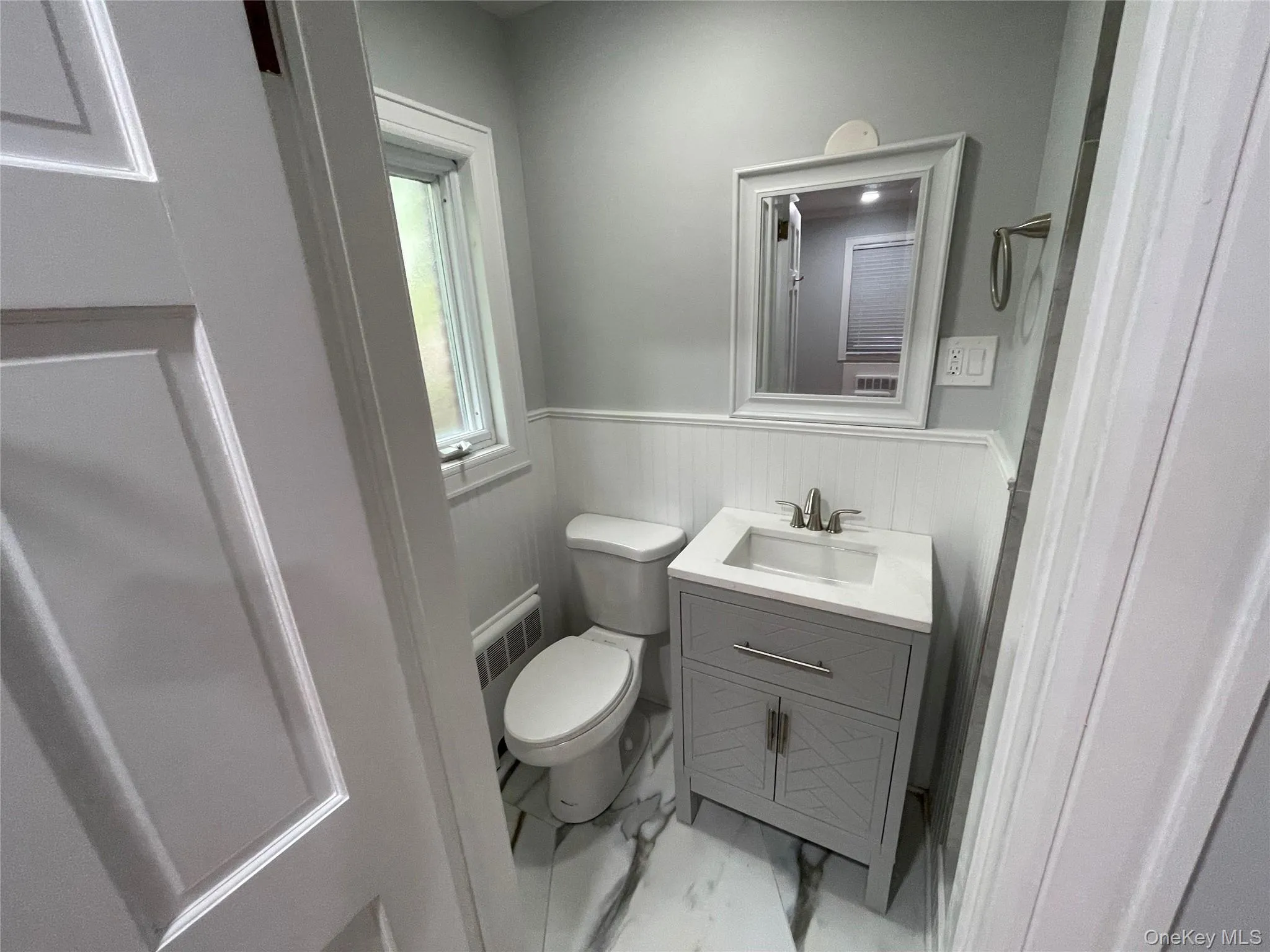 Half bath featuring a wainscoted wall, radiator heating unit, light marble finish flooring, and vanity Half bath featuring a wainscoted wall, radiator heating unit, light marble finish flooring, and vanity