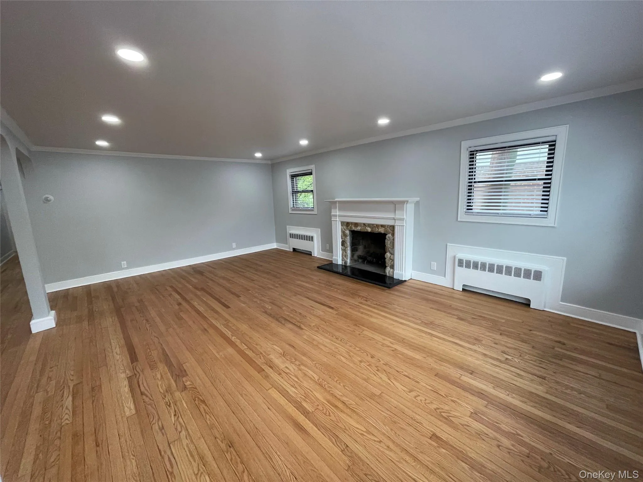 Unfurnished living room with crown molding, recessed lighting, radiator, a premium fireplace, and light wood-style floors Unfurnished living room with crown molding, recessed lighting, radiator, a premium fireplace, and light wood-style floors
