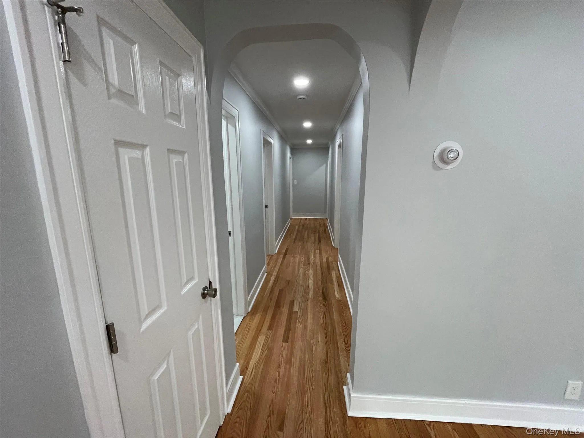 Corridor featuring arched walkways, wood finished floors, and crown molding Corridor featuring arched walkways, wood finished floors, and crown molding