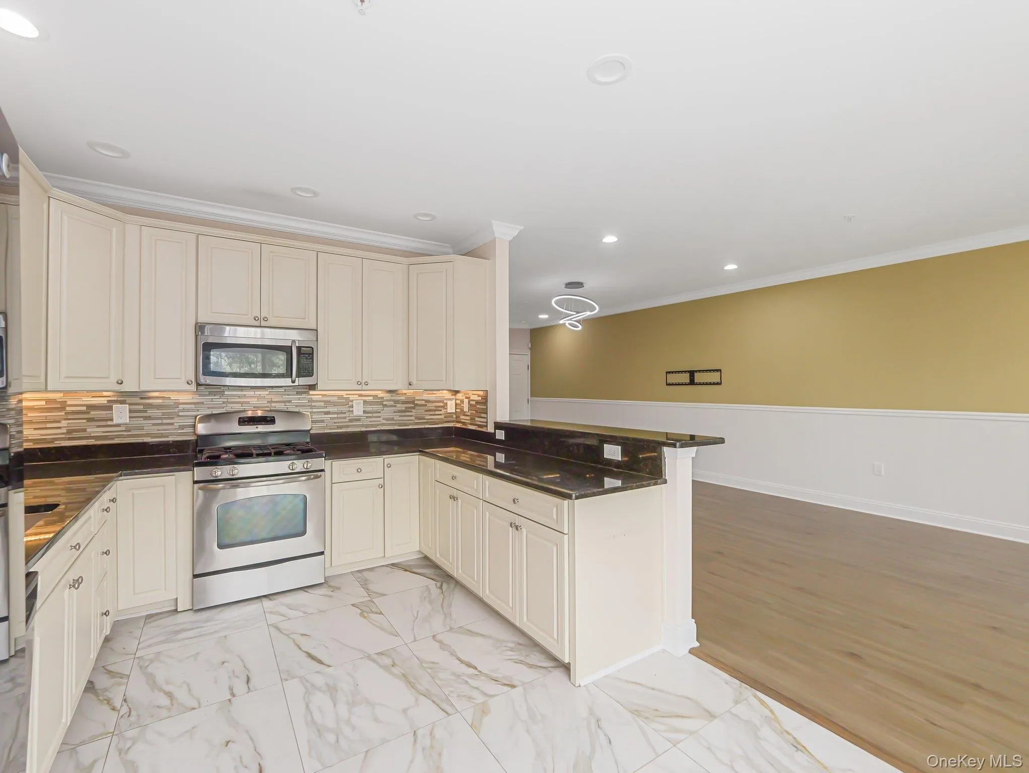 Kitchen featuring appliances with stainless steel finishes, cream cabinets, light marble finish floors, a peninsula, and ornamental molding Kitchen featuring appliances with stainless steel finishes, cream cabinets, light marble finish floors, a peninsula, and ornamental molding