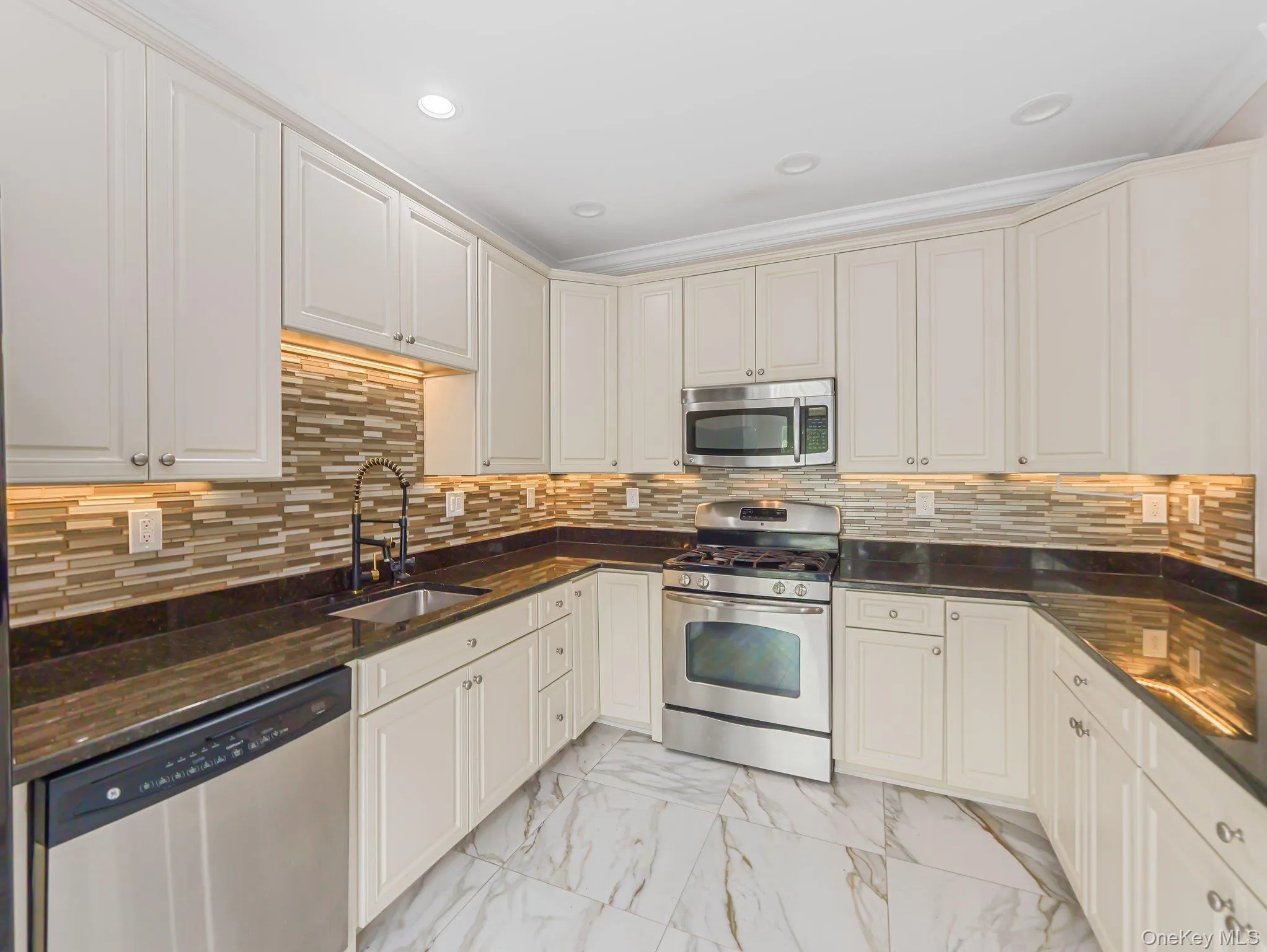 Kitchen featuring stainless steel appliances, light marble finish floors, tasteful backsplash, dark stone countertops, and recessed lighting Kitchen featuring stainless steel appliances, light marble finish floors, tasteful backsplash, dark stone countertops, and recessed lighting