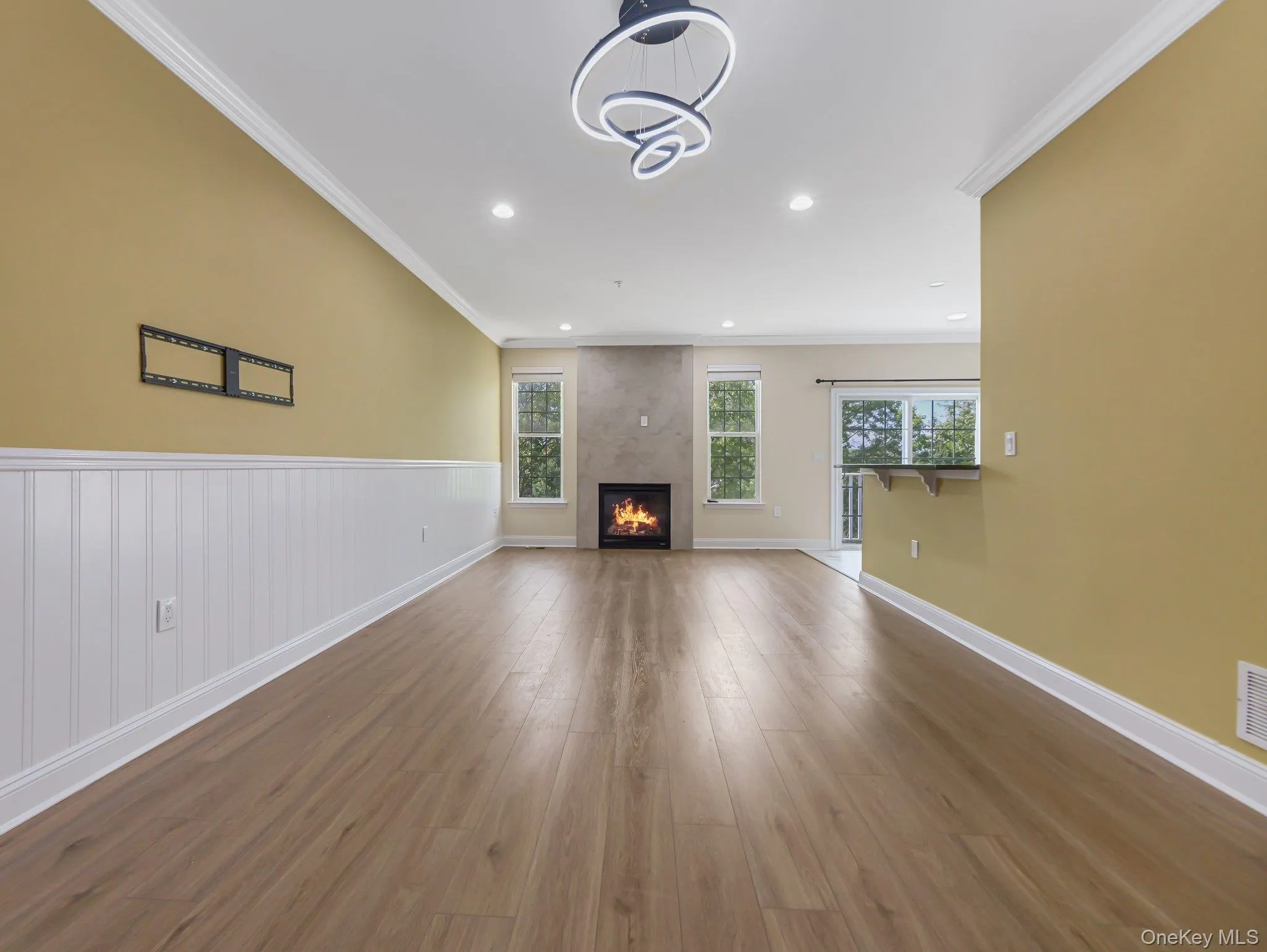 Unfurnished living room featuring ornamental molding, wood finished floors, a fireplace, recessed lighting, and wainscoting Unfurnished living room featuring ornamental molding, wood finished floors, a fireplace, recessed lighting, and wainscoting