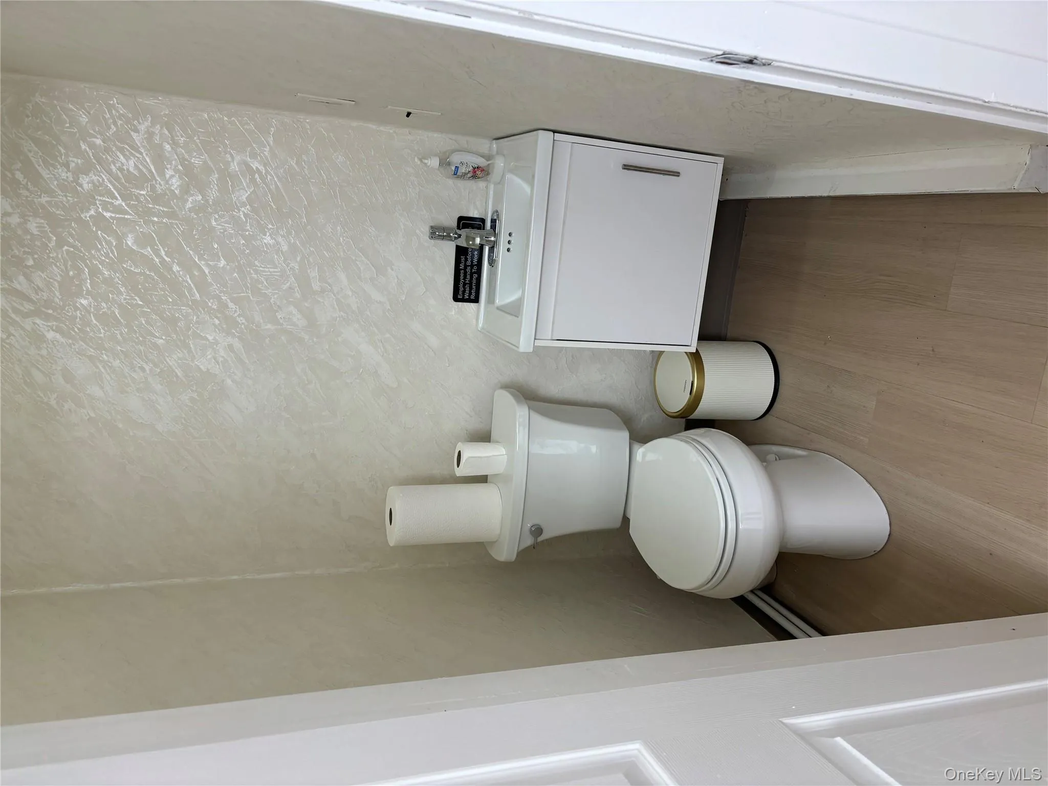 Half bath featuring vanity, light wood-style flooring, a textured wall, and baseboard heating Half bath featuring vanity, light wood-style flooring, a textured wall, and baseboard heating