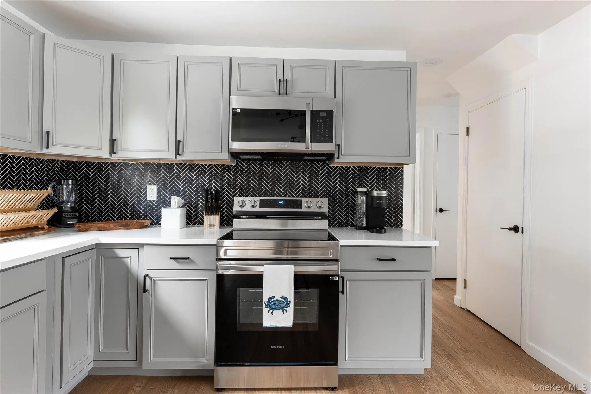 Kitchen with gray cabinetry, stainless steel appliances, backsplash, light wood finished floors, and light stone countertops Kitchen with gray cabinetry, stainless steel appliances, backsplash, light wood finished floors, and light stone countertops