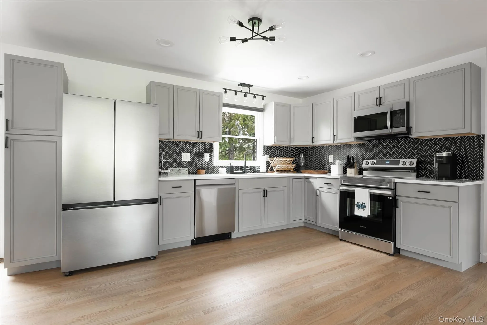 Kitchen featuring gray cabinets, appliances with stainless steel finishes, backsplash, light wood finished floors, and recessed lighting Kitchen featuring gray cabinets, appliances with stainless steel finishes, backsplash, light wood finished floors, and recessed lighting