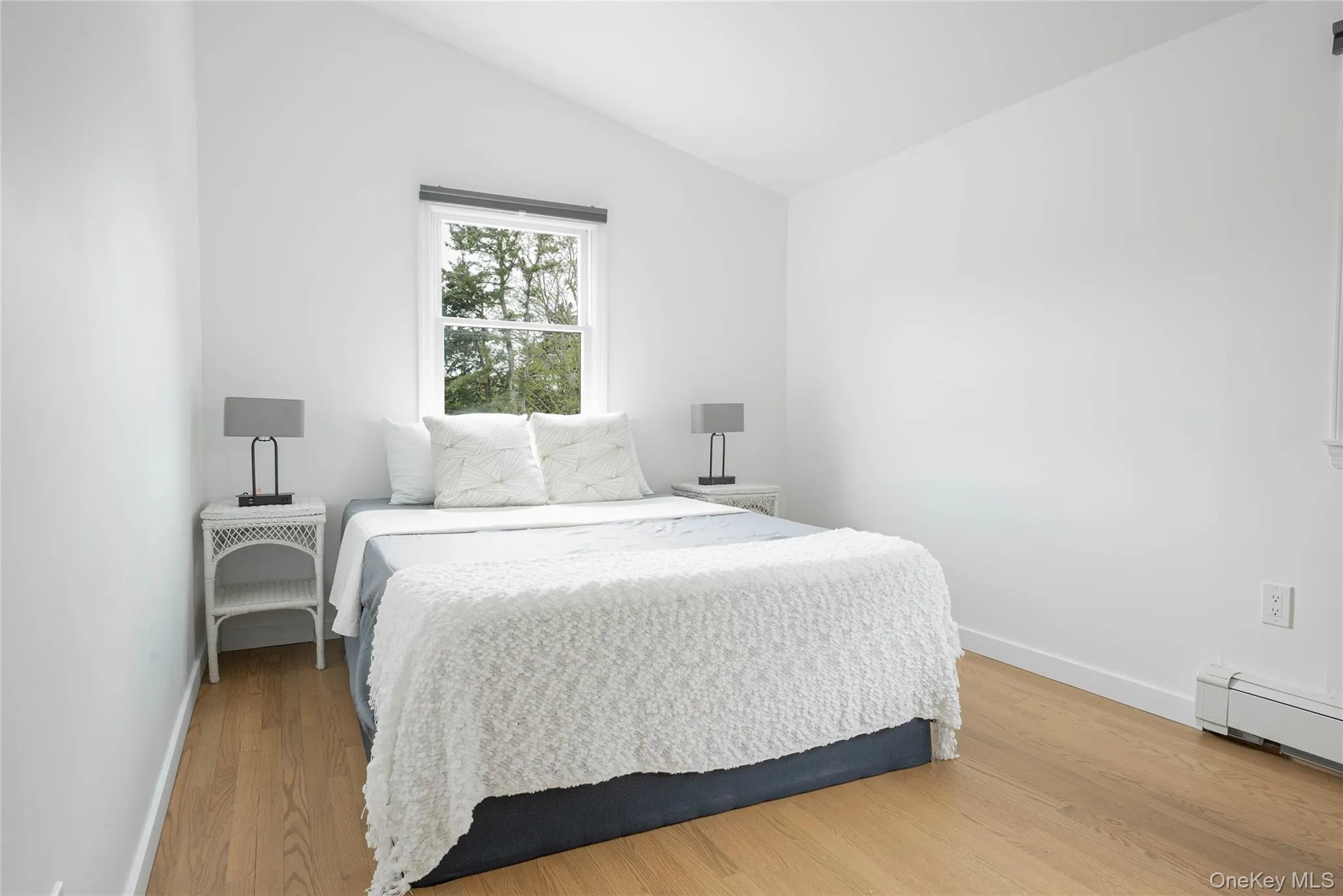 Bedroom with vaulted ceiling, light wood-type flooring, and a baseboard heating unit Bedroom with vaulted ceiling, light wood-type flooring, and a baseboard heating unit