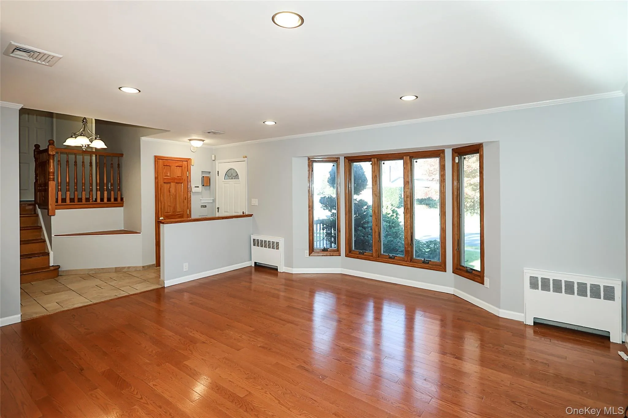 Unfurnished living room with radiator heating unit, stairway, hardwood / wood-style floors, ornamental molding, and recessed lighting Unfurnished living room with radiator heating unit, stairway, hardwood / wood-style floors, ornamental molding, and recessed lighting