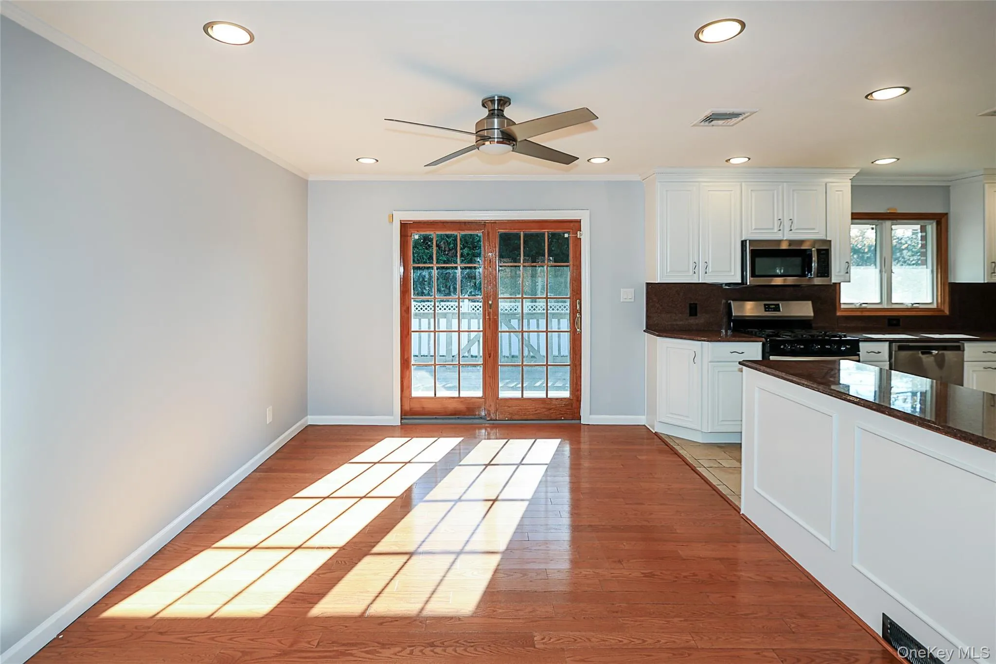 Kitchen featuring white cabinetry, appliances with stainless steel finishes, tasteful backsplash, light wood-type flooring, and ornamental molding Kitchen featuring white cabinetry, appliances with stainless steel finishes, tasteful backsplash, light wood-type flooring, and ornamental molding