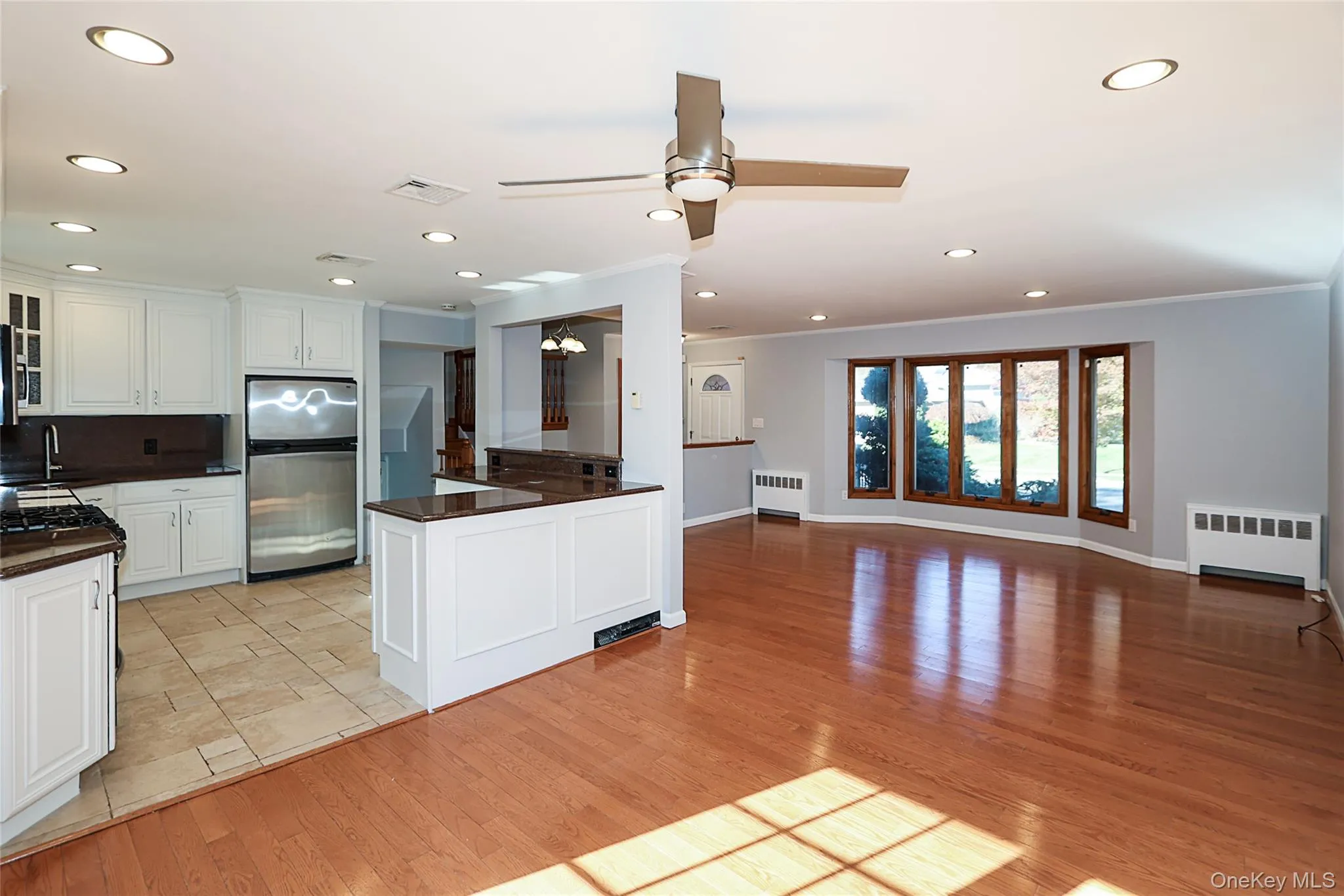 Kitchen with freestanding refrigerator, open floor plan, white cabinetry, a ceiling fan, and radiator Kitchen with freestanding refrigerator, open floor plan, white cabinetry, a ceiling fan, and radiator