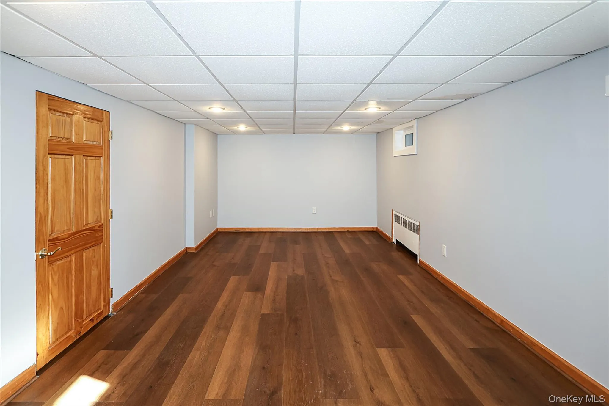 Unfurnished room featuring a paneled ceiling, dark wood-type flooring, and radiator heating unit Unfurnished room featuring a paneled ceiling, dark wood-type flooring, and radiator heating unit