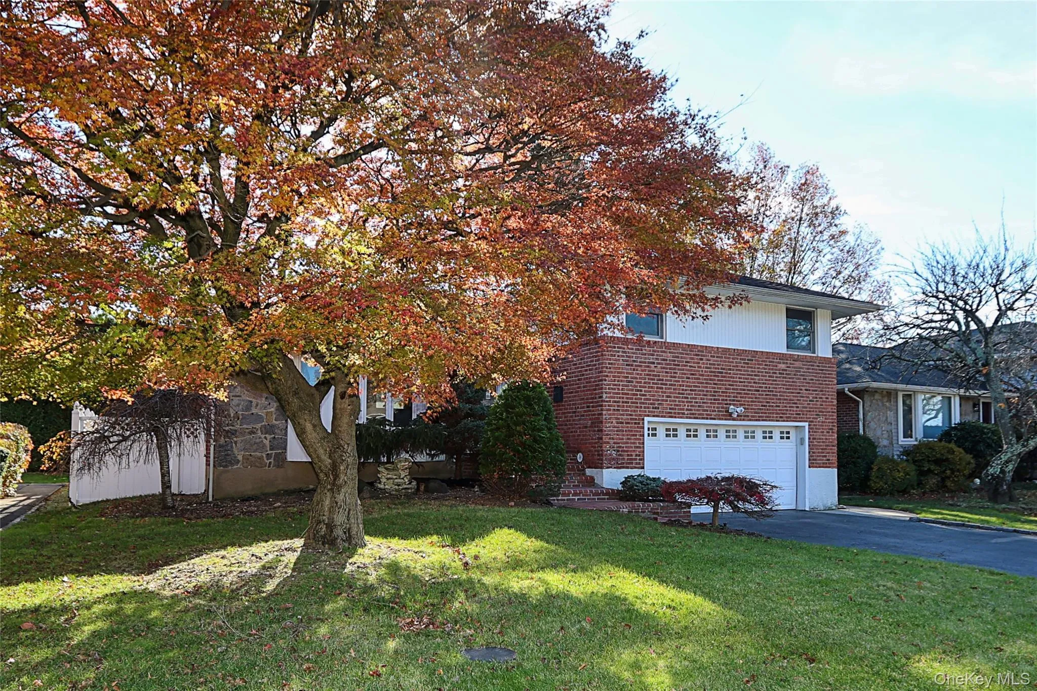 View of side of property featuring a lawn, driveway, a garage, brick siding, and stone siding View of side of property featuring a lawn, driveway, a garage, brick siding, and stone siding