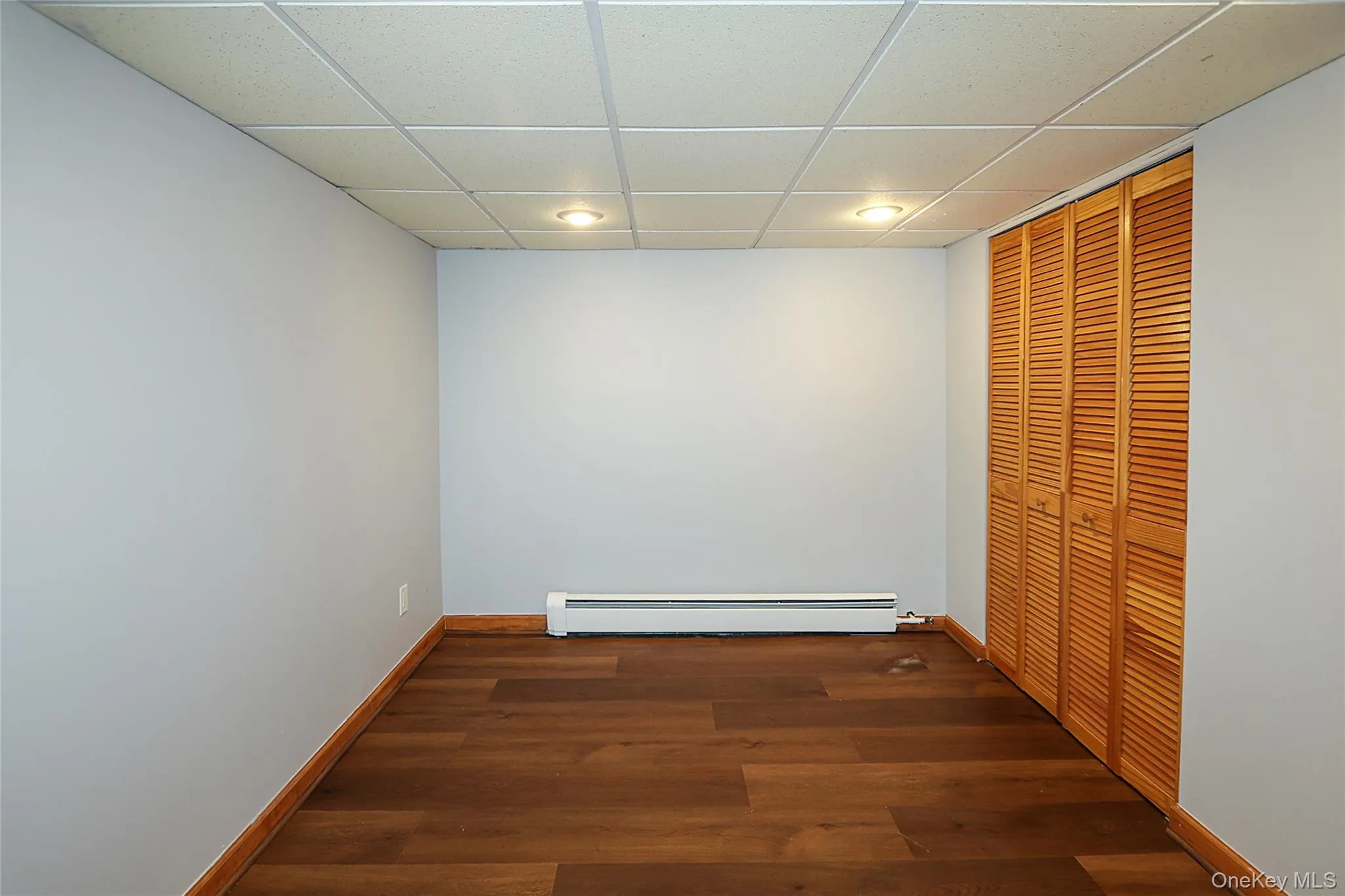 Unfurnished bedroom with a drop ceiling, a closet, dark wood-type flooring, recessed lighting, and baseboard heating Unfurnished bedroom with a drop ceiling, a closet, dark wood-type flooring, recessed lighting, and baseboard heating