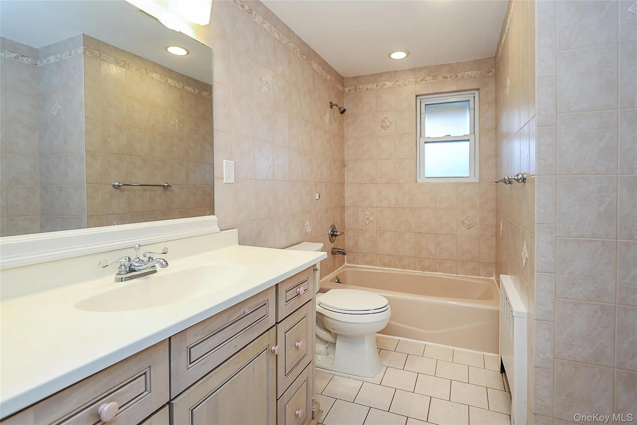 Full bathroom featuring vanity, light tile patterned floors, tile walls, radiator heating unit, and shower / tub combination Full bathroom featuring vanity, light tile patterned floors, tile walls, radiator heating unit, and shower / tub combination