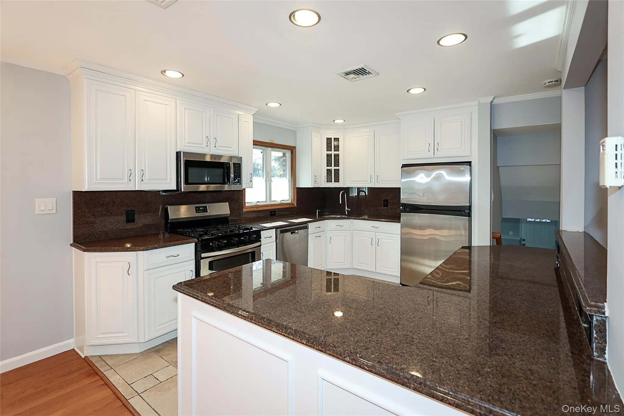 Kitchen with stainless steel appliances, dark stone countertops, white cabinets, ornamental molding, and a peninsula Kitchen with stainless steel appliances, dark stone countertops, white cabinets, ornamental molding, and a peninsula