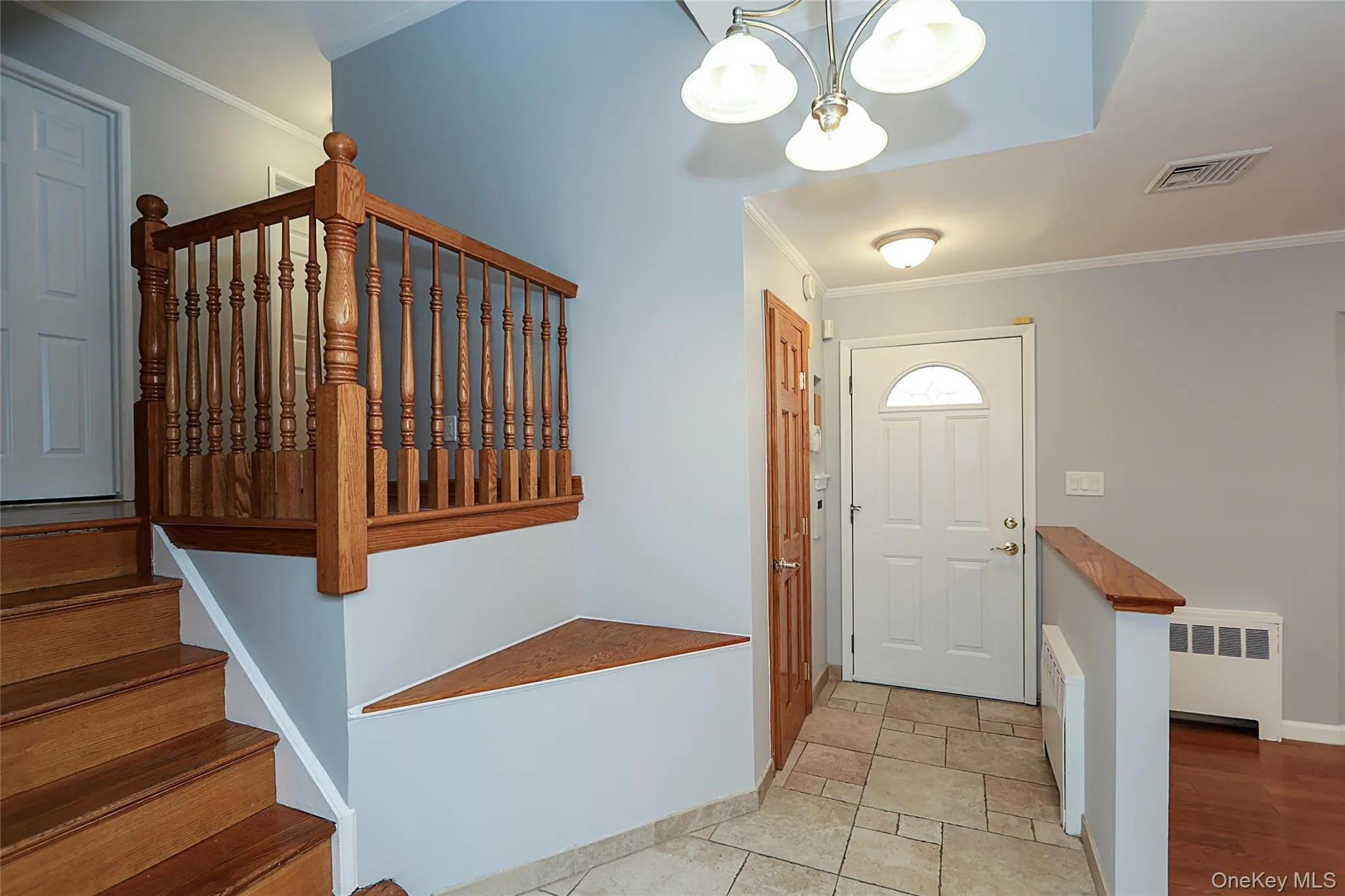 Foyer featuring ornamental molding, stairway, radiator heating unit, and a chandelier Foyer featuring ornamental molding, stairway, radiator heating unit, and a chandelier