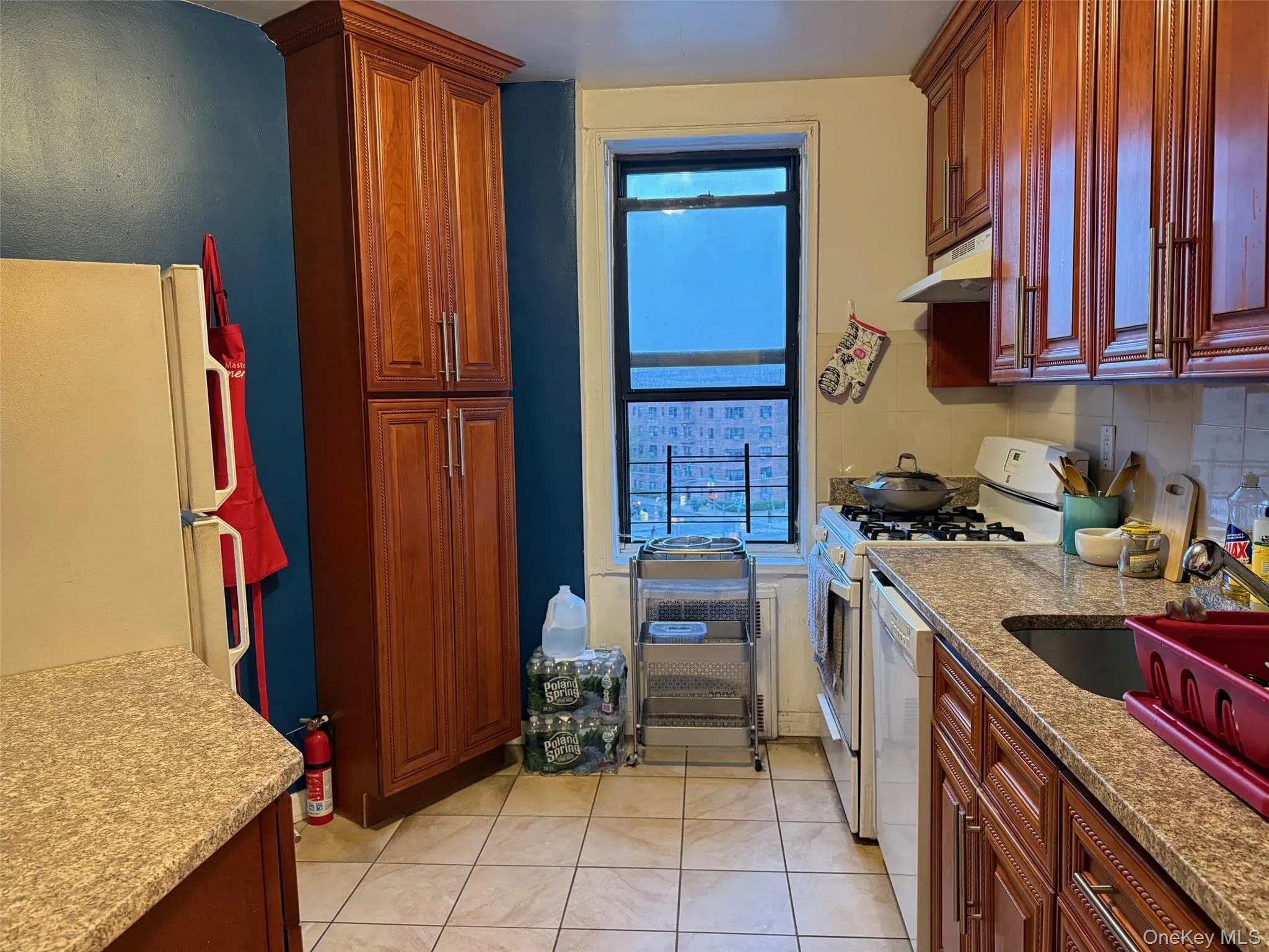 Kitchen with white appliances, light tile patterned flooring, decorative backsplash, light stone countertops, and under cabinet range hood Kitchen with white appliances, light tile patterned flooring, decorative backsplash, light stone countertops, and under cabinet range hood