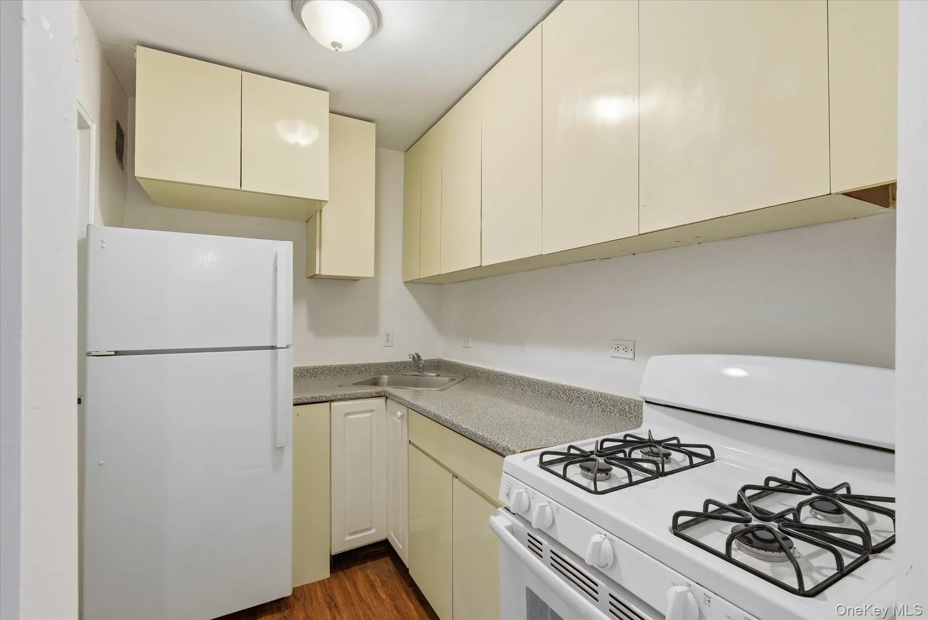 Kitchen with white appliances, cream cabinetry, and dark wood finished floors Kitchen with white appliances, cream cabinetry, and dark wood finished floors