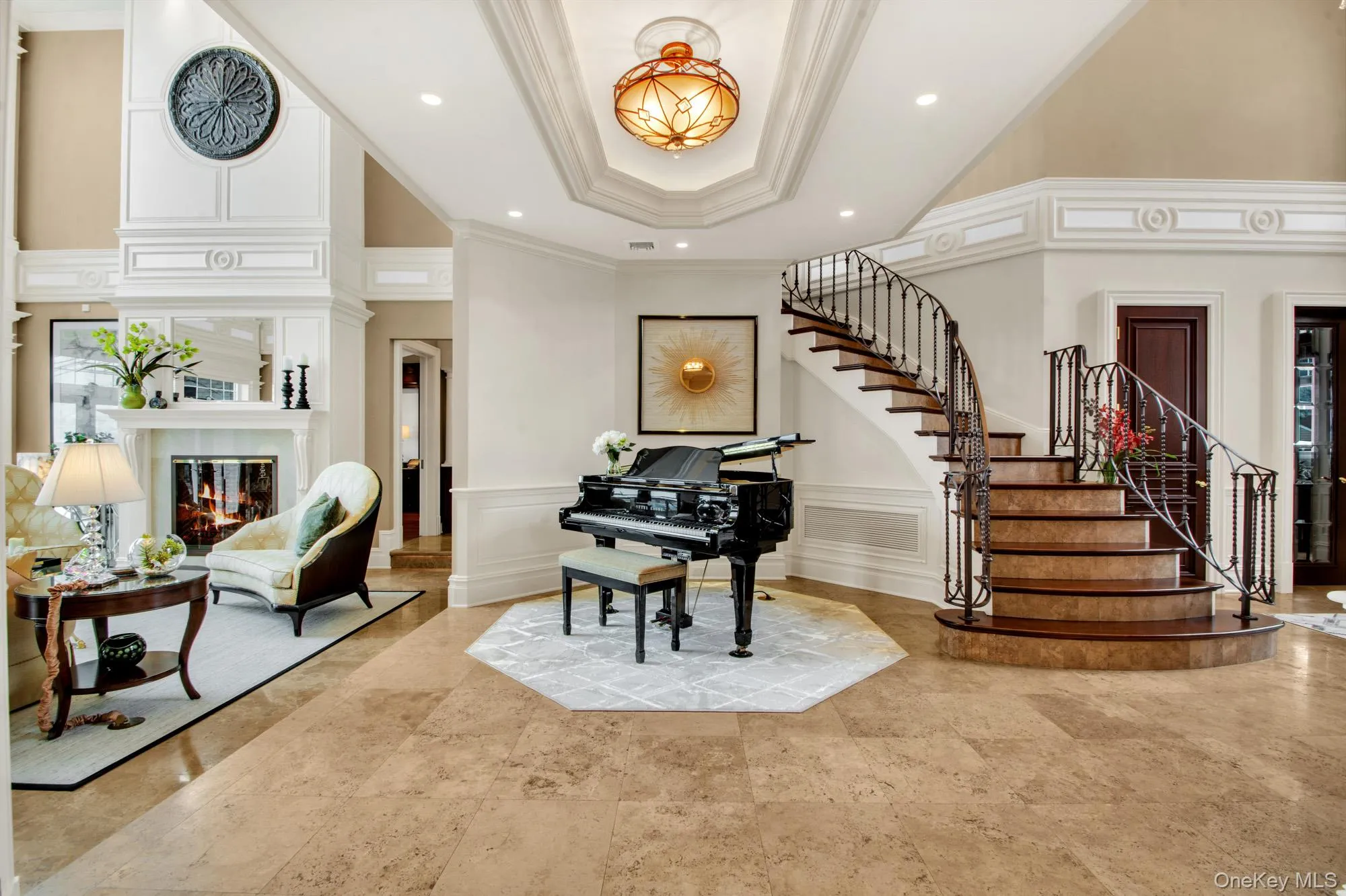 Foyer featuring a decorative wall, a glass covered fireplace, ornamental molding, a tray ceiling, and a towering ceiling Foyer featuring a decorative wall, a glass covered fireplace, ornamental molding, a tray ceiling, and a towering ceiling