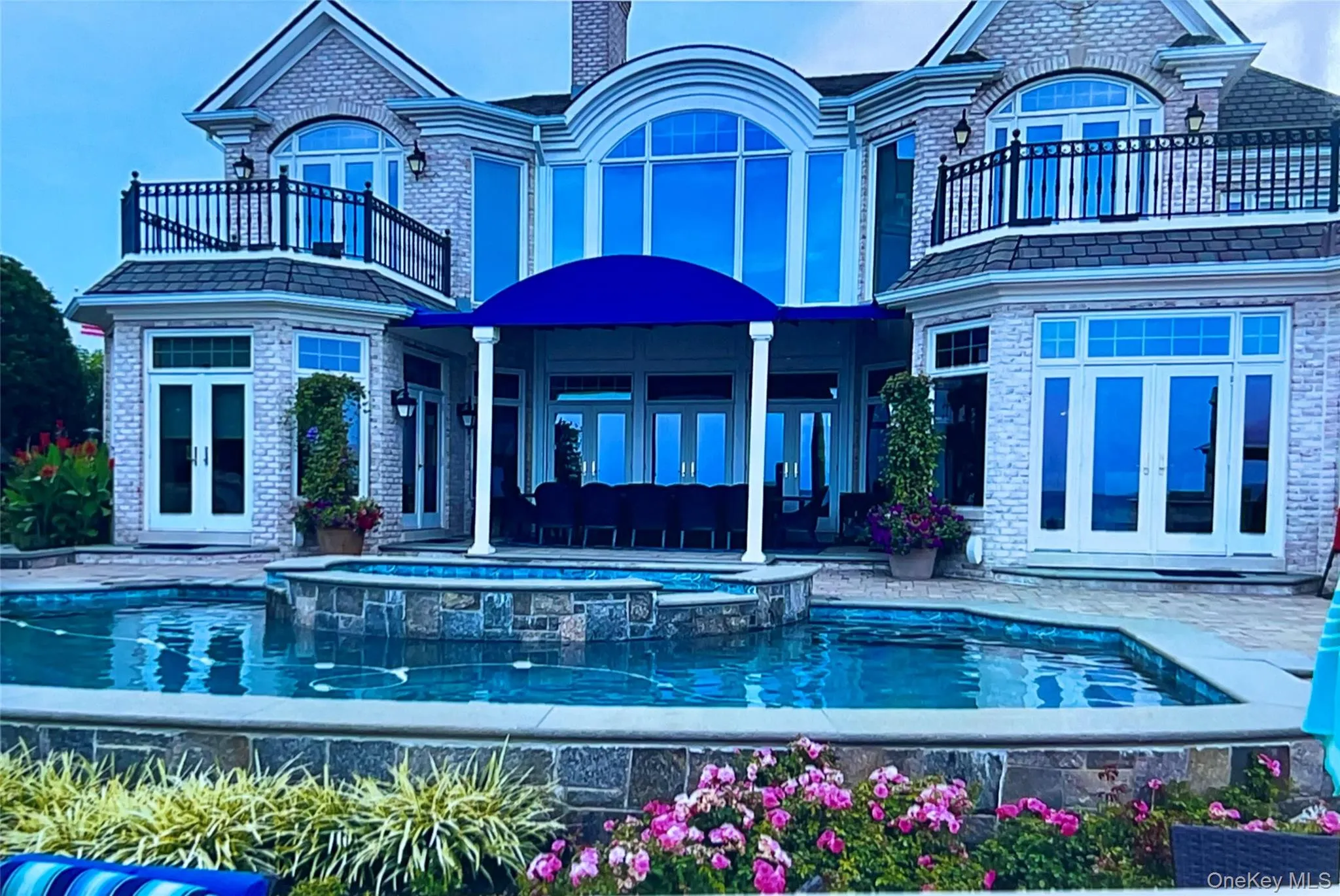 Rear view of property with french doors, a balcony, a patio area, a pool with connected hot tub, and brick siding Rear view of property with french doors, a balcony, a patio area, a pool with connected hot tub, and brick siding