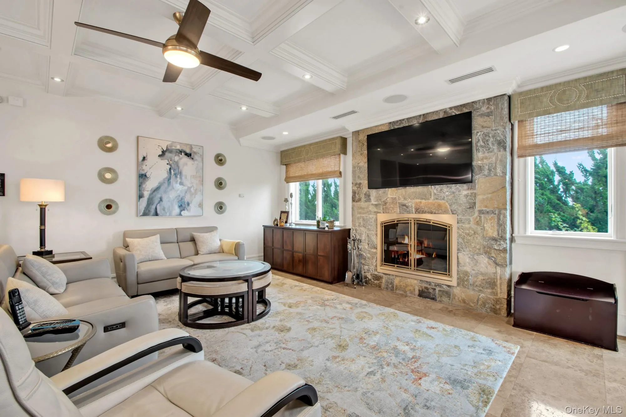 Living room with a stone fireplace, beamed ceiling, a ceiling fan, and coffered ceiling Living room with a stone fireplace, beamed ceiling, a ceiling fan, and coffered ceiling