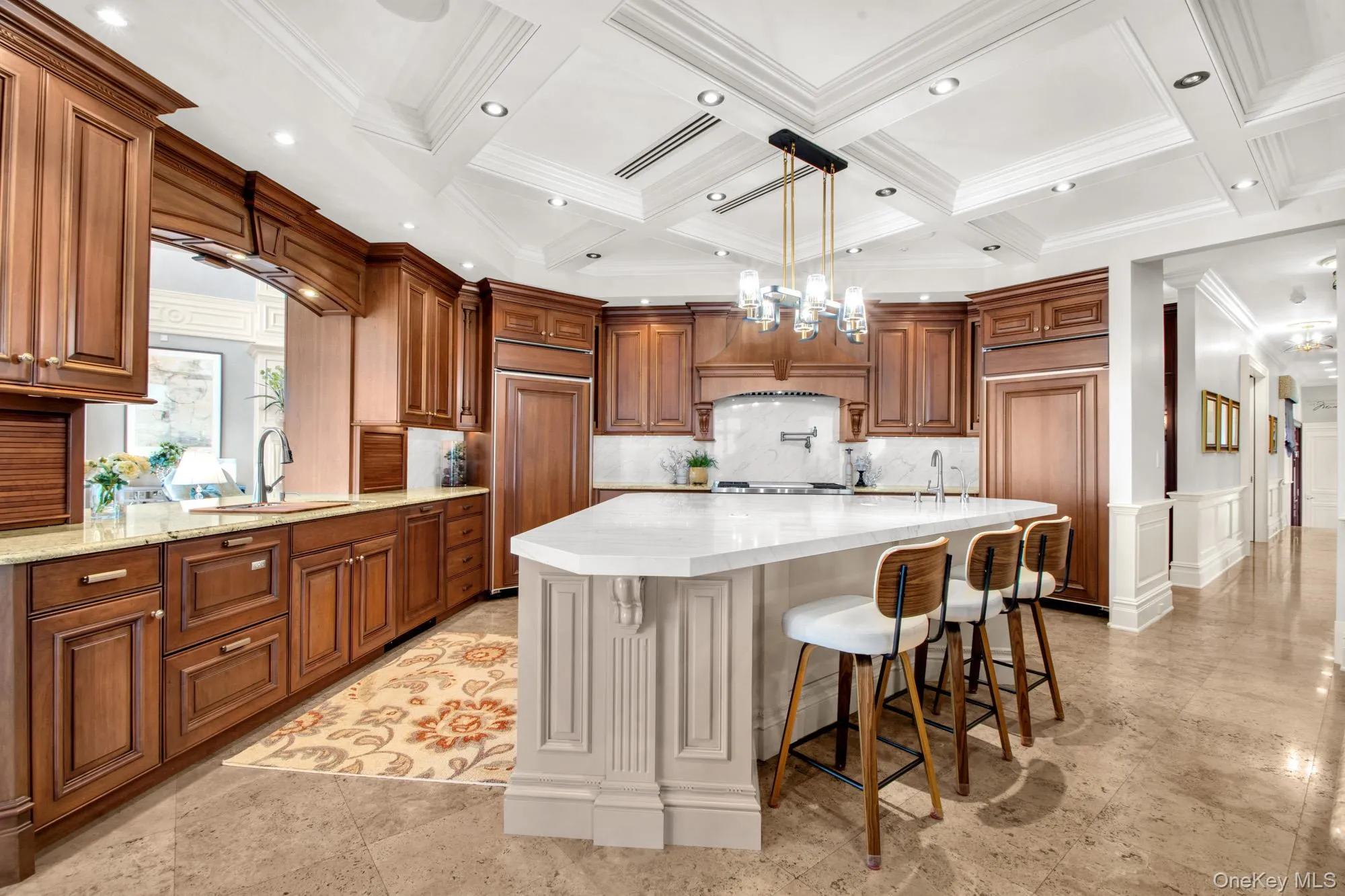 Kitchen featuring a chandelier, brown cabinetry, a kitchen bar, pendant lighting, and light stone counters Kitchen featuring a chandelier, brown cabinetry, a kitchen bar, pendant lighting, and light stone counters