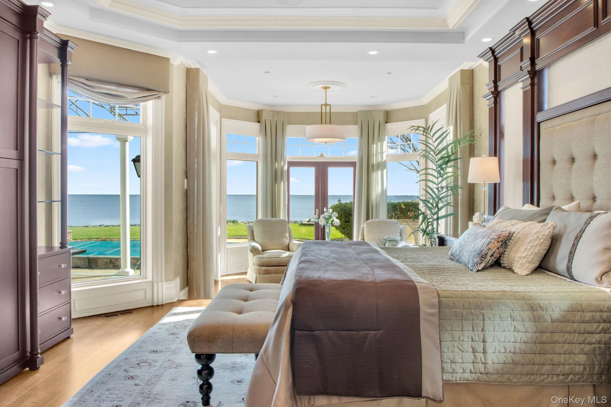 Bedroom featuring french doors, crown molding, a water view, light wood-type flooring, and a tray ceiling Bedroom featuring french doors, crown molding, a water view, light wood-type flooring, and a tray ceiling