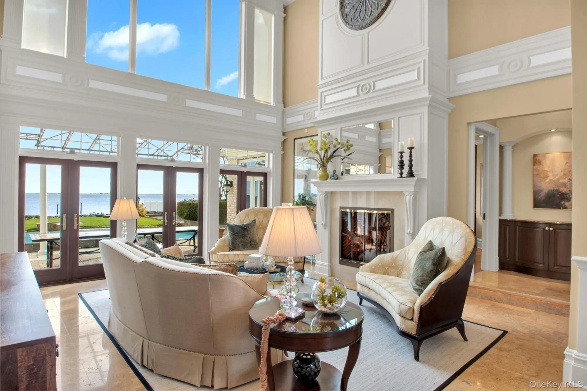 Living room featuring a water view, a towering ceiling, french doors, and a premium fireplace Living room featuring a water view, a towering ceiling, french doors, and a premium fireplace