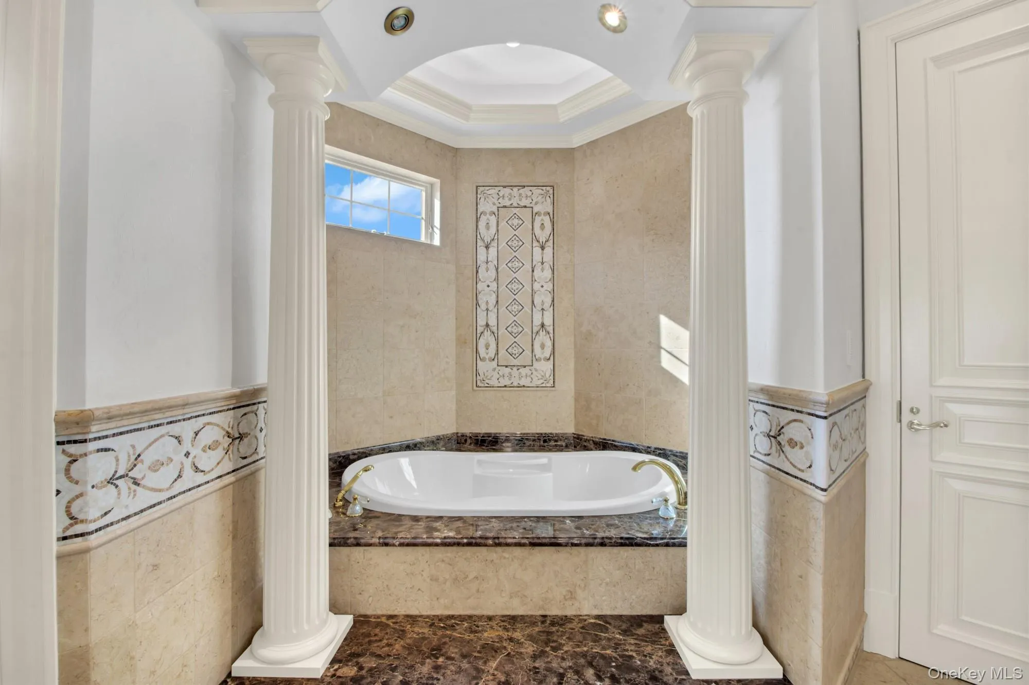 Bathroom with tile walls, a bath, ornate columns, and crown molding Bathroom with tile walls, a bath, ornate columns, and crown molding