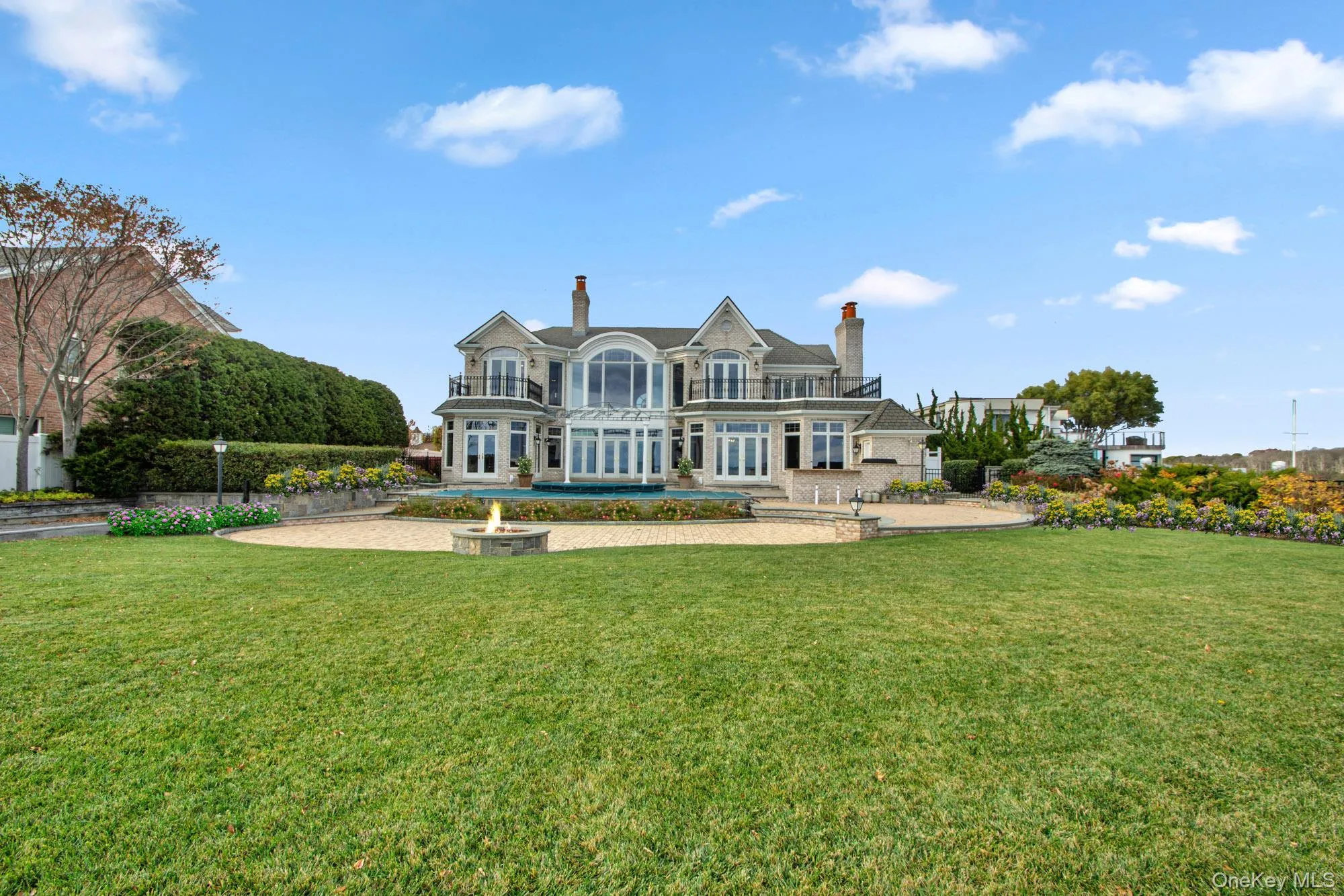 Back of house featuring a chimney, french doors, a patio area, an outdoor fire pit, and a balcony Back of house featuring a chimney, french doors, a patio area, an outdoor fire pit, and a balcony