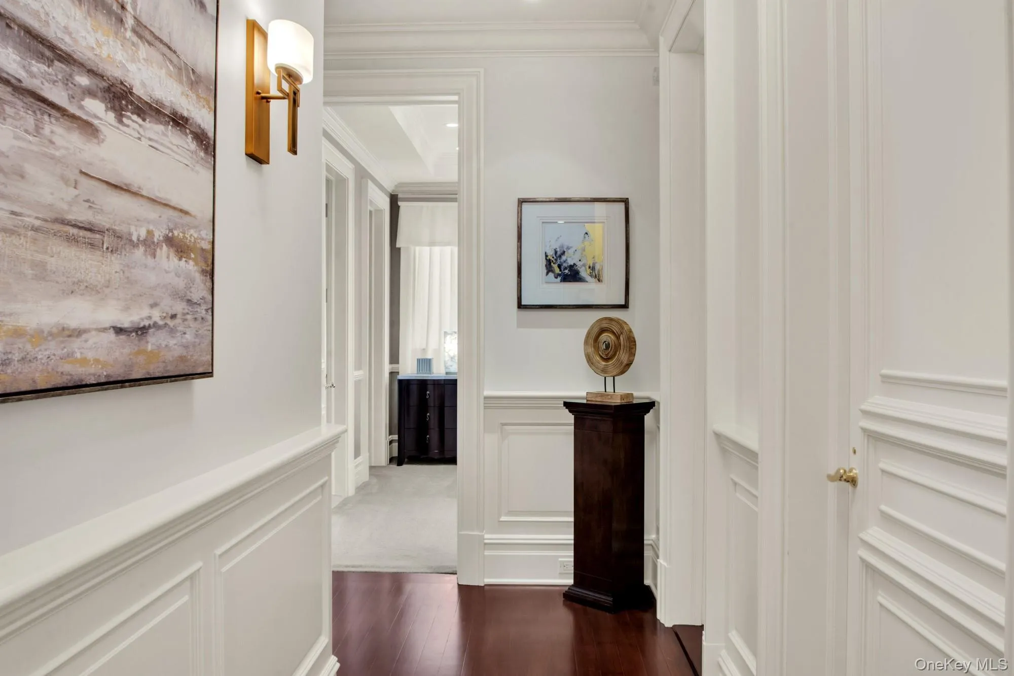 Hallway with crown molding, dark wood-style floors, wainscoting, and a decorative wall Hallway with crown molding, dark wood-style floors, wainscoting, and a decorative wall
