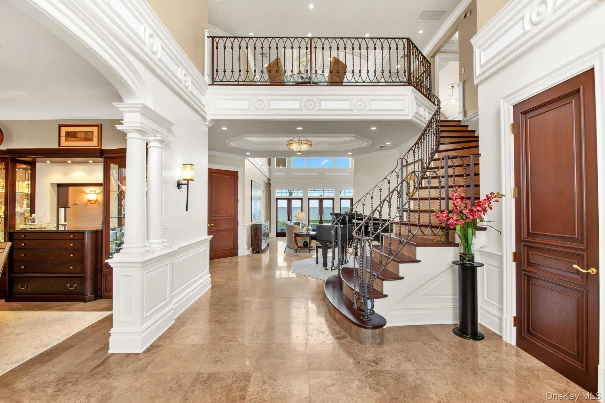 Bright 2 story entry foyer with a decorative wall, stairs, a high ceiling, crown molding, and ornate columns Bright 2 story entry foyer with a decorative wall, stairs, a high ceiling, crown molding, and ornate columns