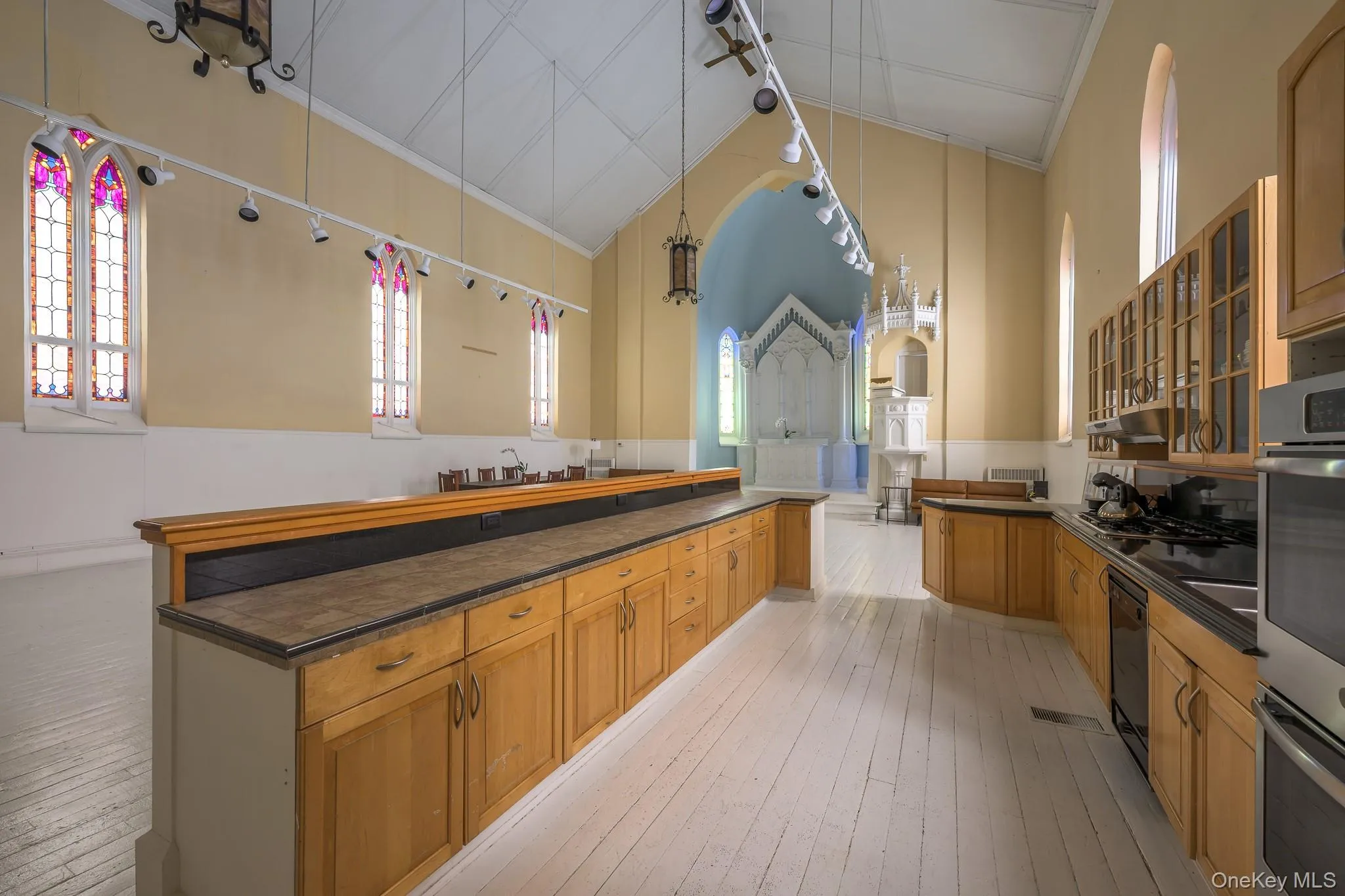 Kitchen with pendant lighting, light wood-style floors, lofted ceiling, and brown cabinetry Kitchen with pendant lighting, light wood-style floors, lofted ceiling, and brown cabinetry