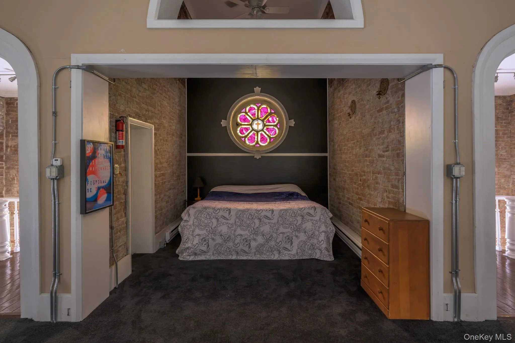 Bedroom with dark carpet, arched walkways, baseboard heating, and brick wall Bedroom with dark carpet, arched walkways, baseboard heating, and brick wall