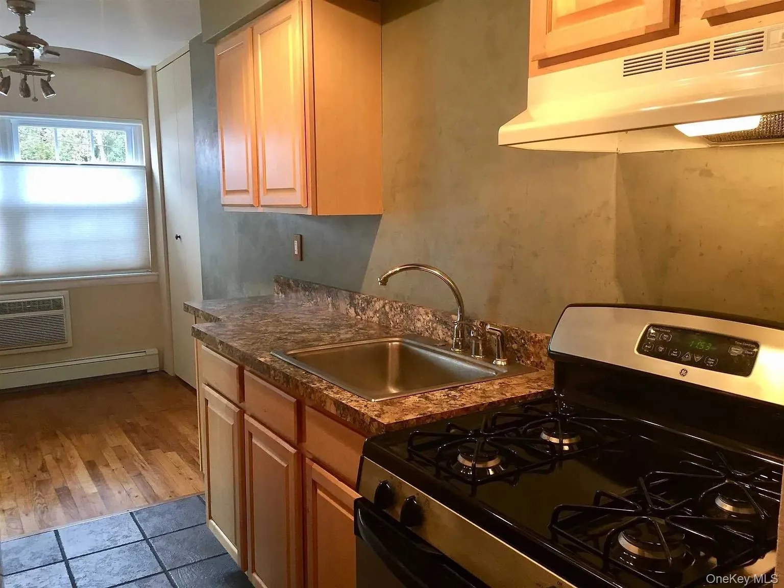 Kitchen with stainless steel gas stove, under cabinet range hood, dark countertops, ceiling fan, and baseboard heating Kitchen with stainless steel gas stove, under cabinet range hood, dark countertops, ceiling fan, and baseboard heating