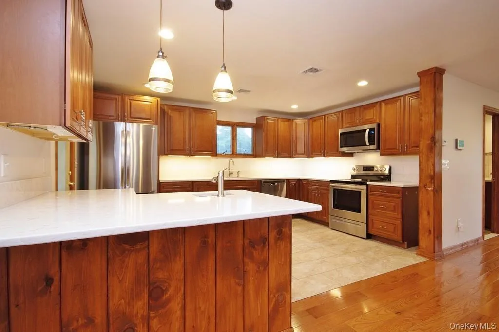 Kitchen featuring a peninsula, brown cabinets, stainless steel appliances, pendant lighting, and recessed lighting Kitchen featuring a peninsula, brown cabinets, stainless steel appliances, pendant lighting, and recessed lighting