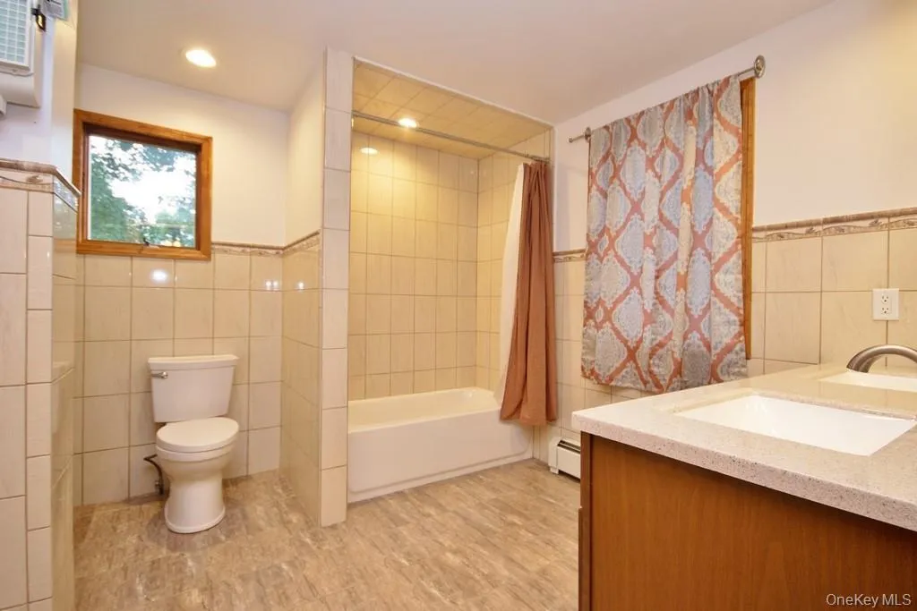 Bathroom featuring tile walls, double vanity, wainscoting, shower / bath combo, and recessed lighting Bathroom featuring tile walls, double vanity, wainscoting, shower / bath combo, and recessed lighting