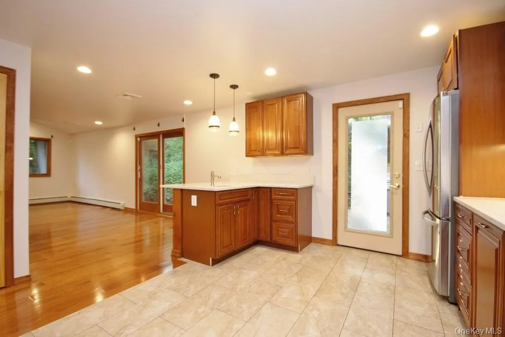 Kitchen with brown cabinetry, pendant lighting, recessed lighting, freestanding refrigerator, and a peninsula Kitchen with brown cabinetry, pendant lighting, recessed lighting, freestanding refrigerator, and a peninsula