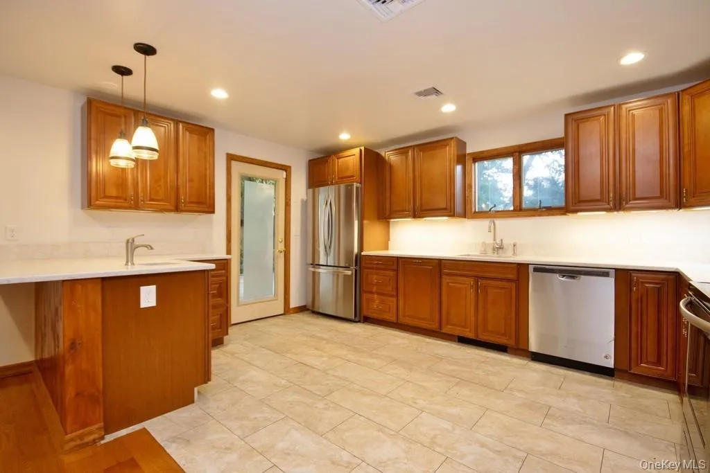 Kitchen featuring brown cabinets, hanging light fixtures, stainless steel appliances, recessed lighting, and light stone countertops Kitchen featuring brown cabinets, hanging light fixtures, stainless steel appliances, recessed lighting, and light stone countertops