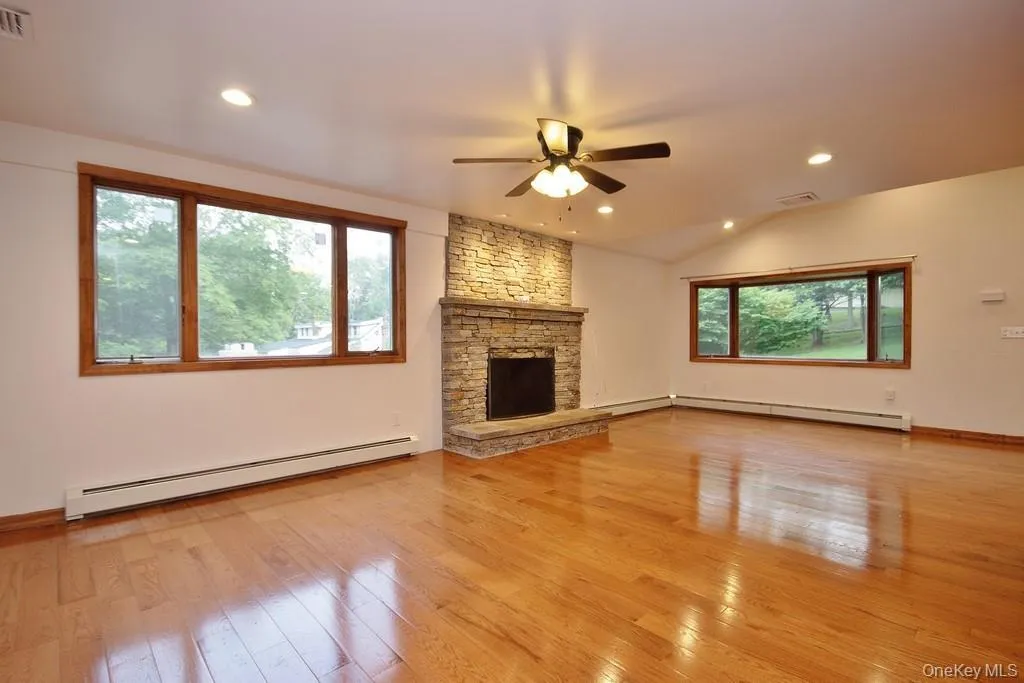 Unfurnished living room with baseboard heating, light wood finished floors, a stone fireplace, recessed lighting, and a ceiling fan Unfurnished living room with baseboard heating, light wood finished floors, a stone fireplace, recessed lighting, and a ceiling fan