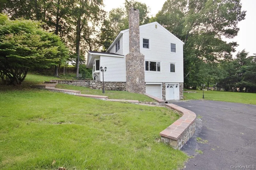 View of side of property with a lawn, asphalt driveway, view of wooded area, and a chimney View of side of property with a lawn, asphalt driveway, view of wooded area, and a chimney