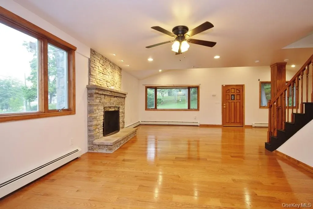 Unfurnished living room featuring a baseboard heating unit, stairs, light wood finished floors, lofted ceiling, and recessed lighting Unfurnished living room featuring a baseboard heating unit, stairs, light wood finished floors, lofted ceiling, and recessed lighting