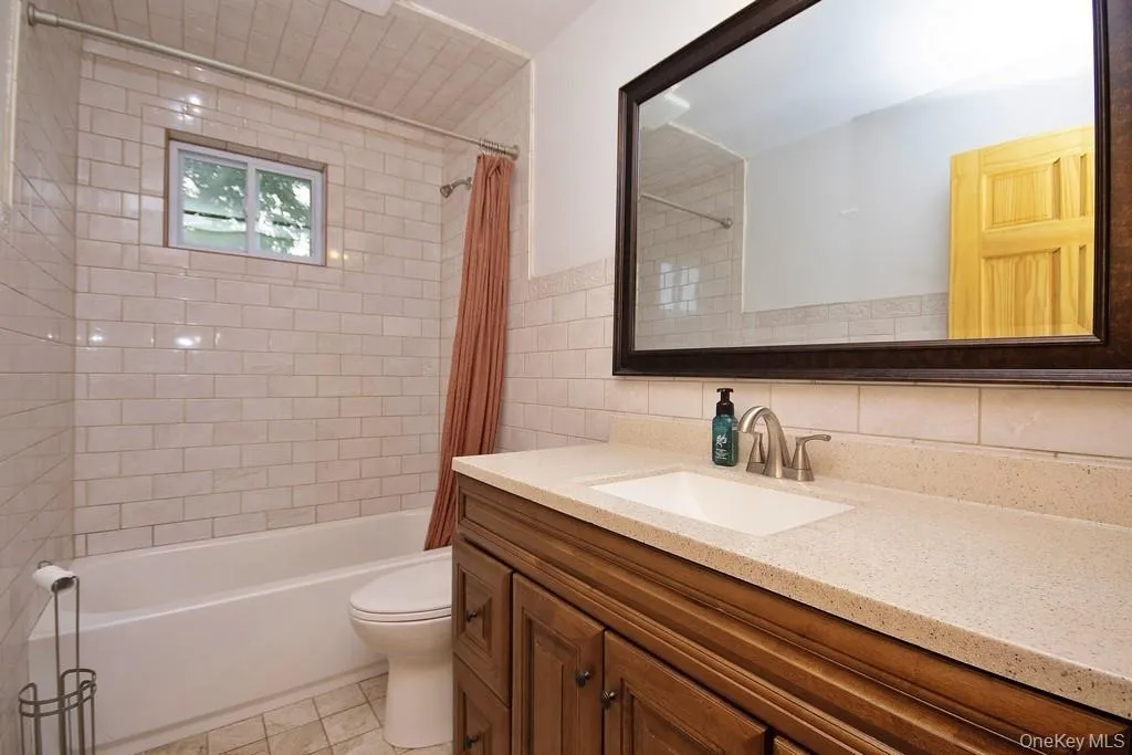 Full bathroom with shower / tub combo with curtain, vanity, light tile patterned floors, tasteful backsplash, and tile walls Full bathroom with shower / tub combo with curtain, vanity, light tile patterned floors, tasteful backsplash, and tile walls