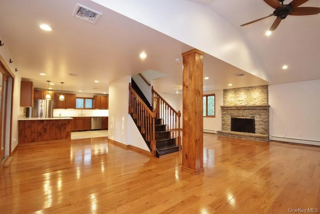 Unfurnished living room featuring recessed lighting, light wood finished floors, a stone fireplace, a ceiling fan, and stairway Unfurnished living room featuring recessed lighting, light wood finished floors, a stone fireplace, a ceiling fan, and stairway
