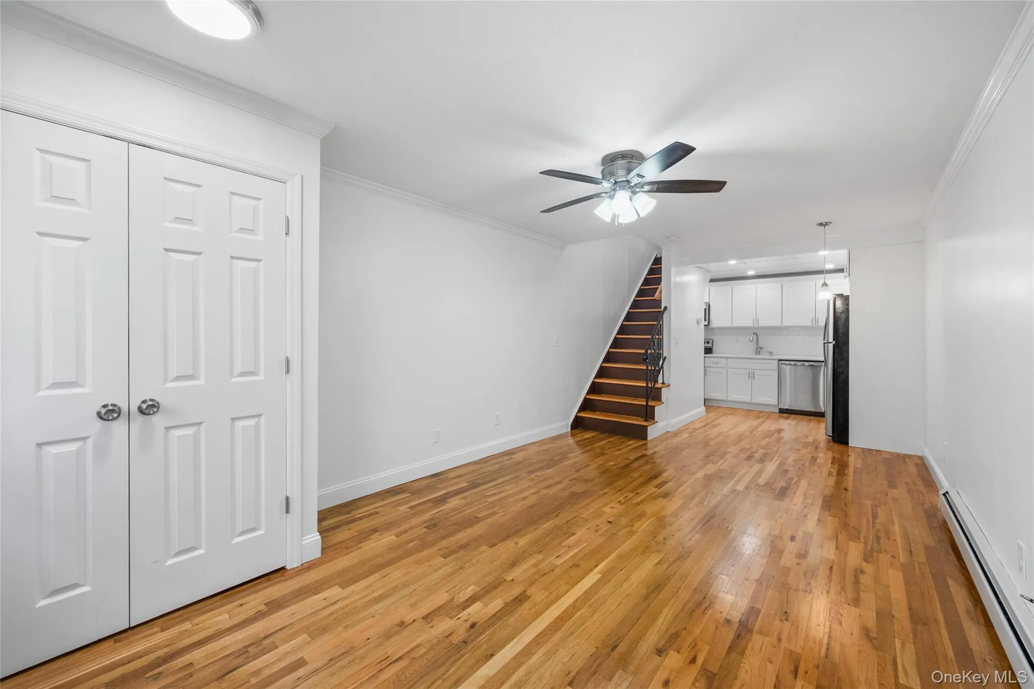 Unfurnished living room featuring stairs, a baseboard radiator, crown molding, light wood finished floors, and a ceiling fan Unfurnished living room featuring stairs, a baseboard radiator, crown molding, light wood finished floors, and a ceiling fan