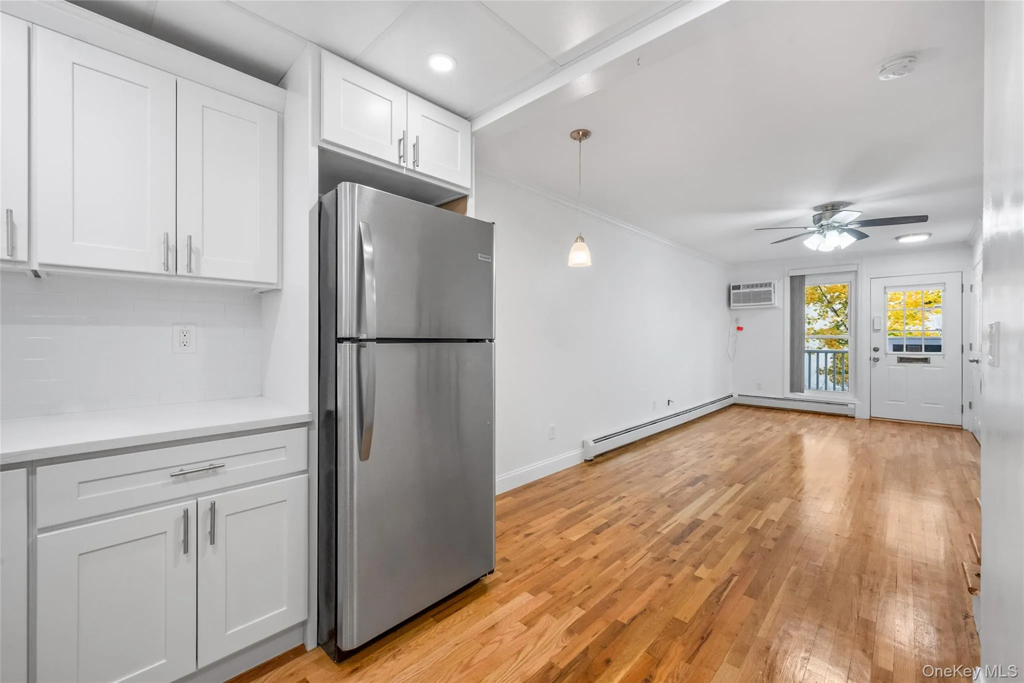 Kitchen featuring freestanding refrigerator, white cabinets, light wood-style flooring, crown molding, and decorative light fixtures Kitchen featuring freestanding refrigerator, white cabinets, light wood-style flooring, crown molding, and decorative light fixtures